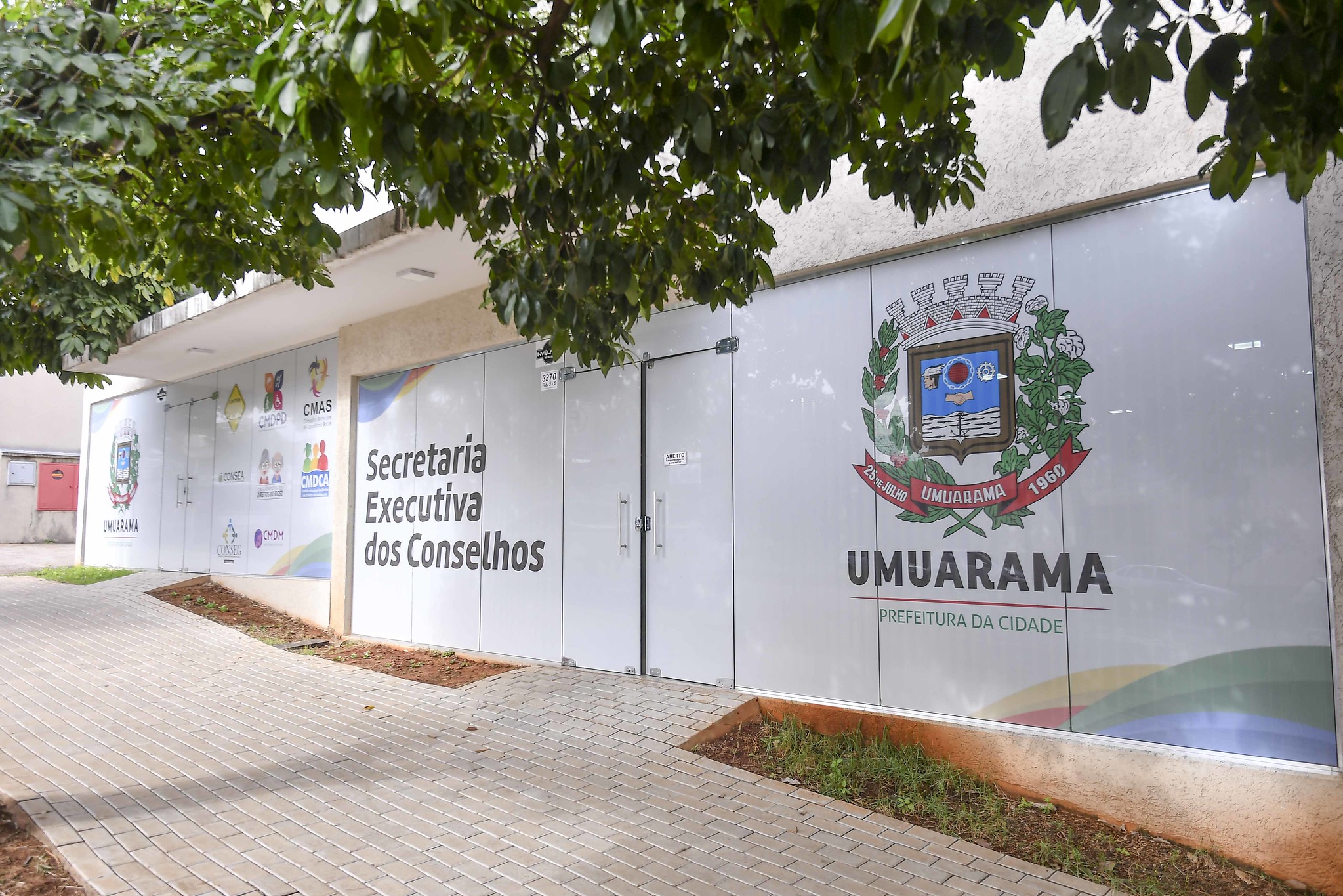 Imagem da fachada envidraçada da Secretaria Executiva dos Conselhos, estampada com o brasão do município de Umuarama