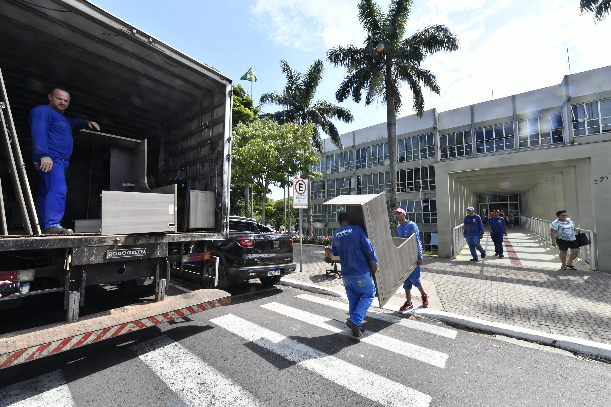 na imagem, servidores transportam móveis de caminhão até o prédio da prefeitura