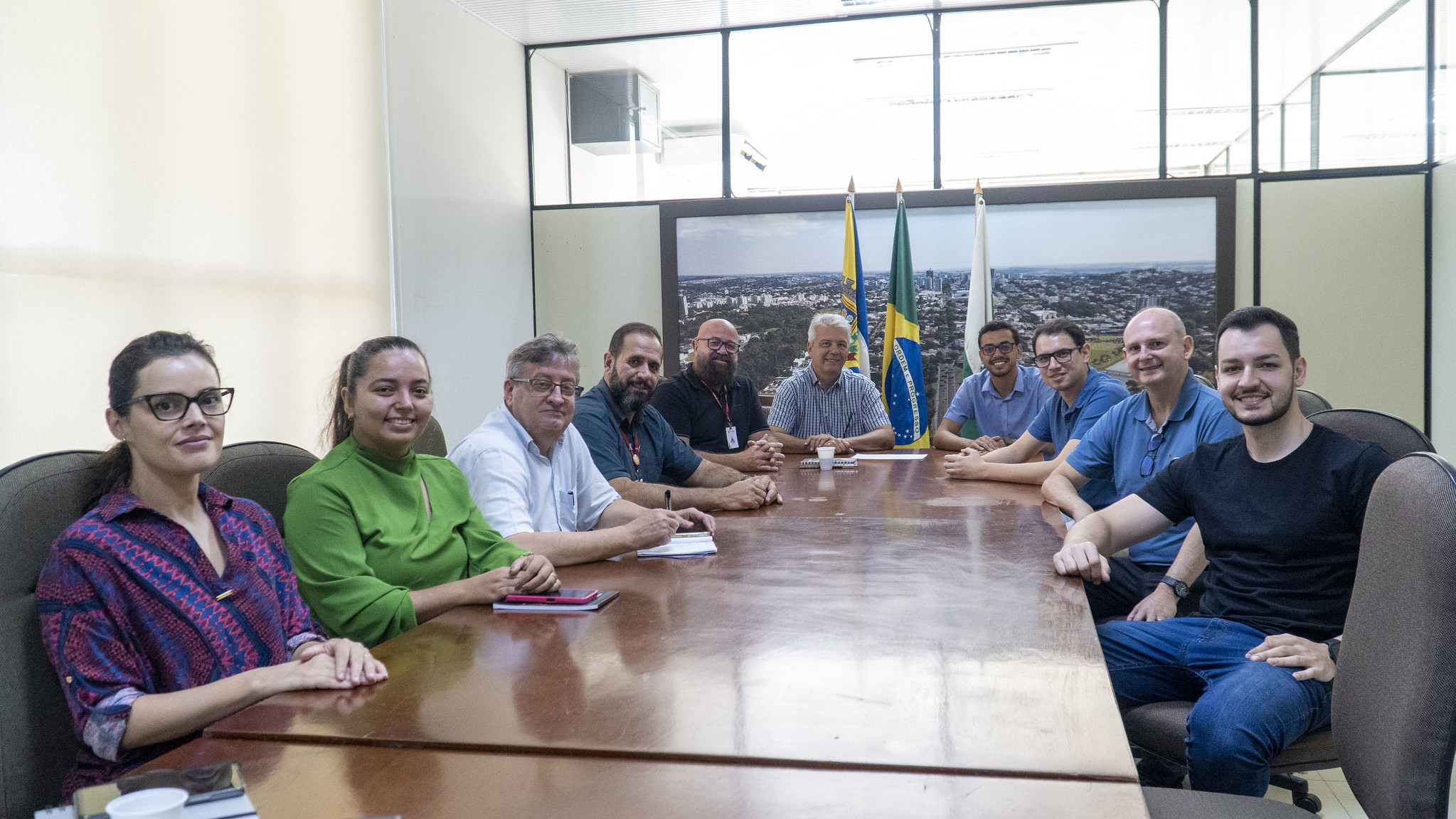 Participantes da reunião reunidos em volta de uma mesa posam para foto