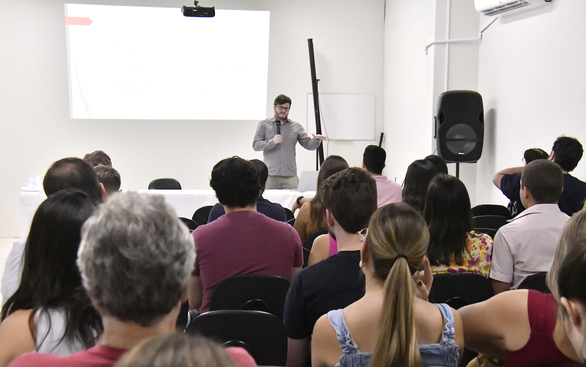 médico fala para publico sentado em sala de reuniões