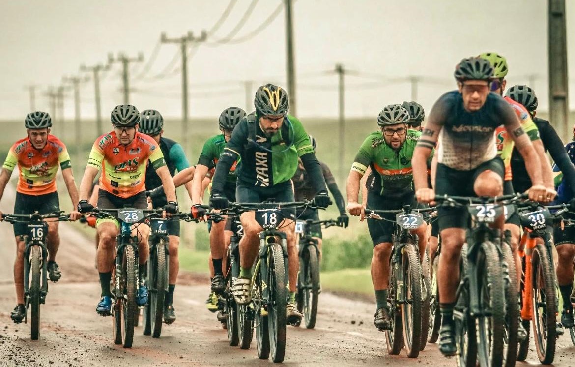 ciclistas pedalam em estrada rural sob a chuva
