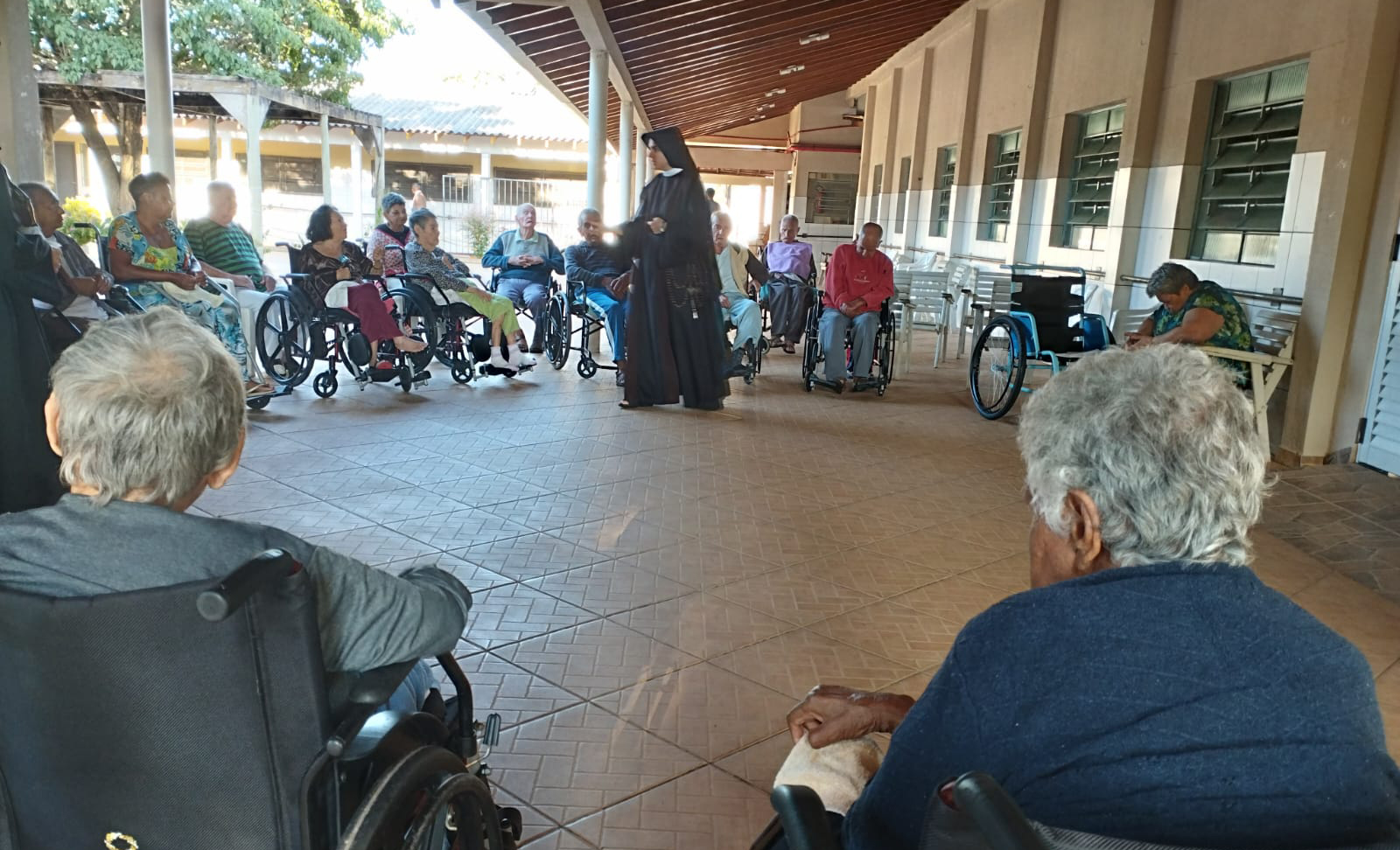 imagem aberta do lar do idoso, com internos sentados e uma irmã religiosa ao centro