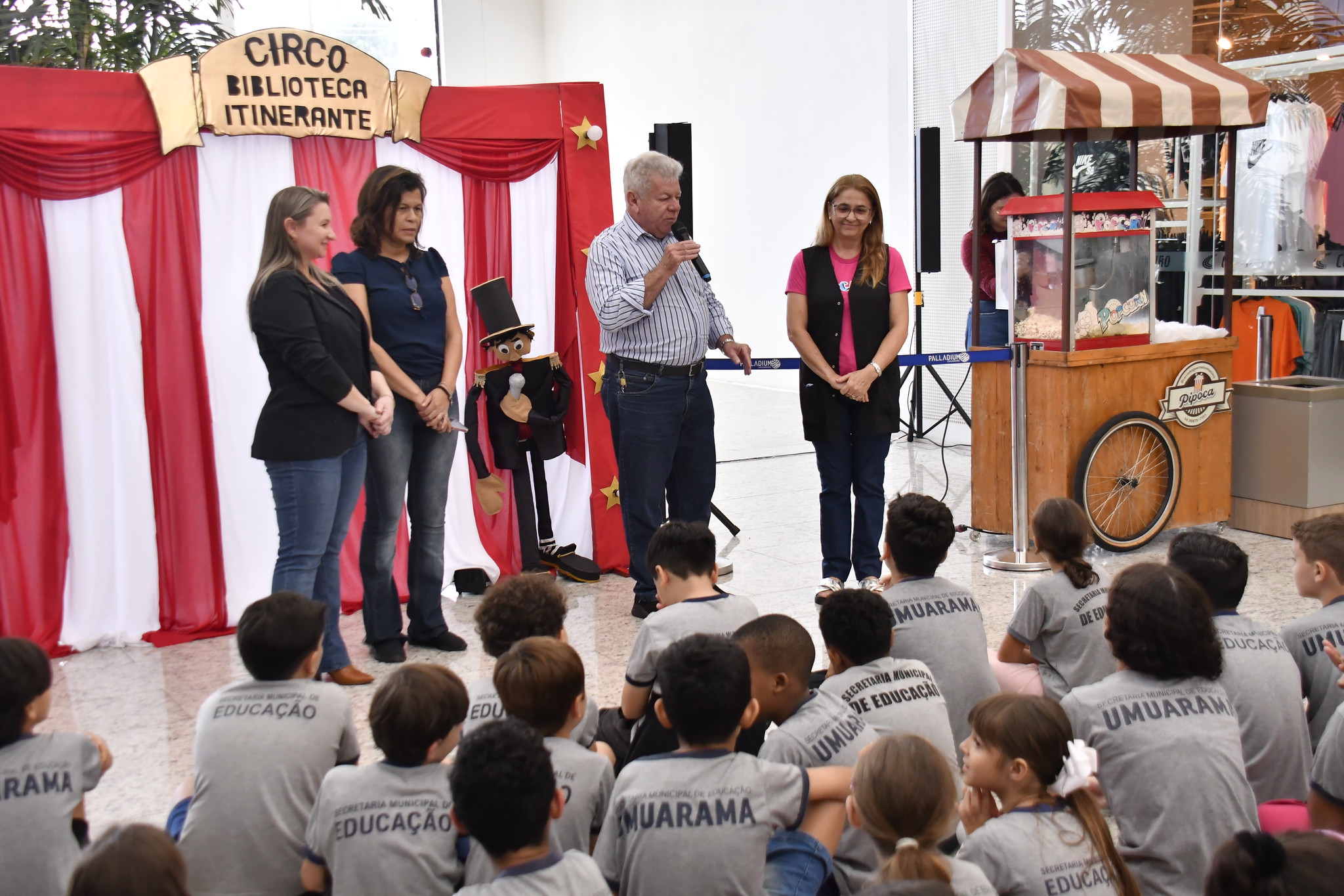 Prefeito e professoras falam para a plateia de alunos diante do palco do teatro de bonecos
