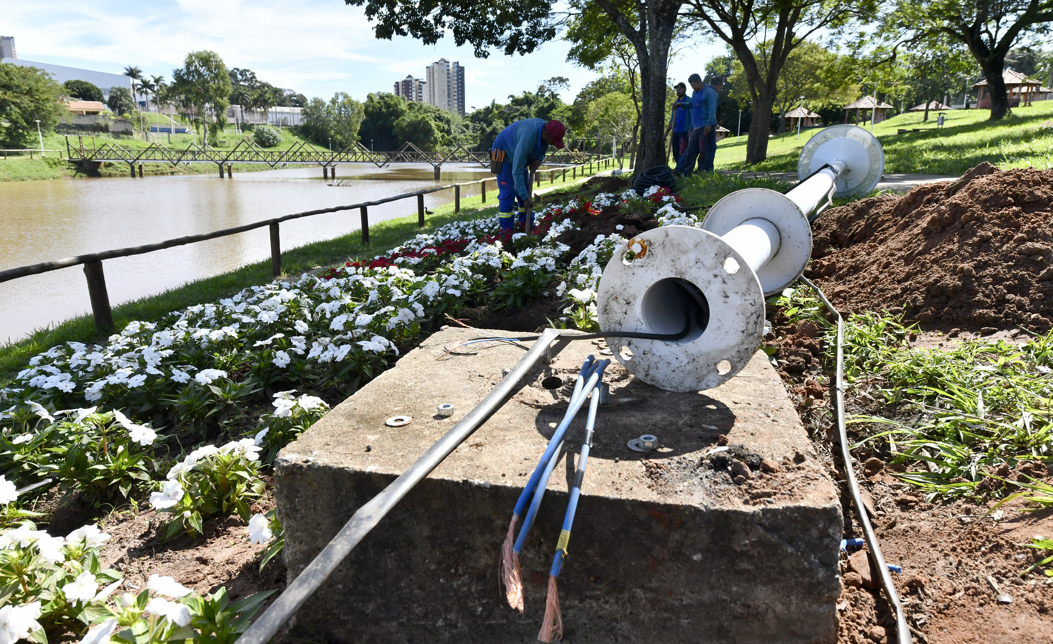 operários reinstalam fiação em poste com luminária LED na margem do lago