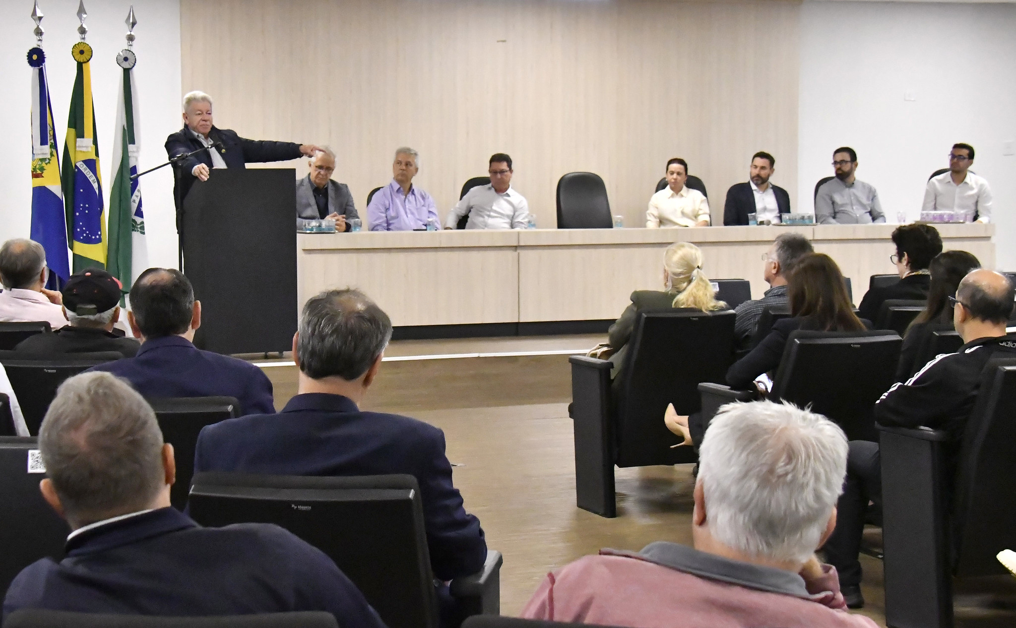 Prefeito discursa na abertura da conferência, diante de autoridades na mesa e o público na plateia
