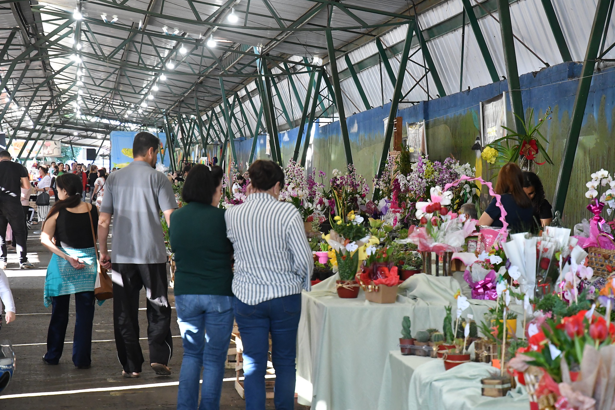 Pessoas caminhando na feira do ano passado, observando flores