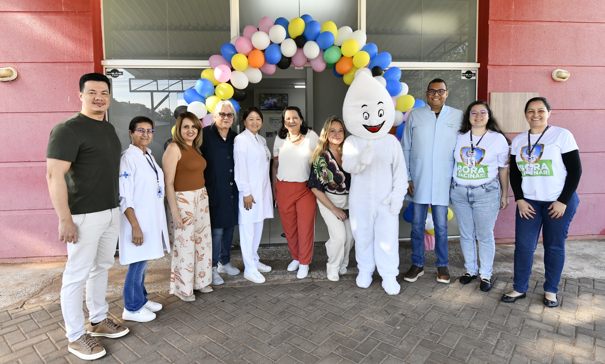 secretária da saúde e equipe posam para foto em unidade de saúde com boneco zé gotinha