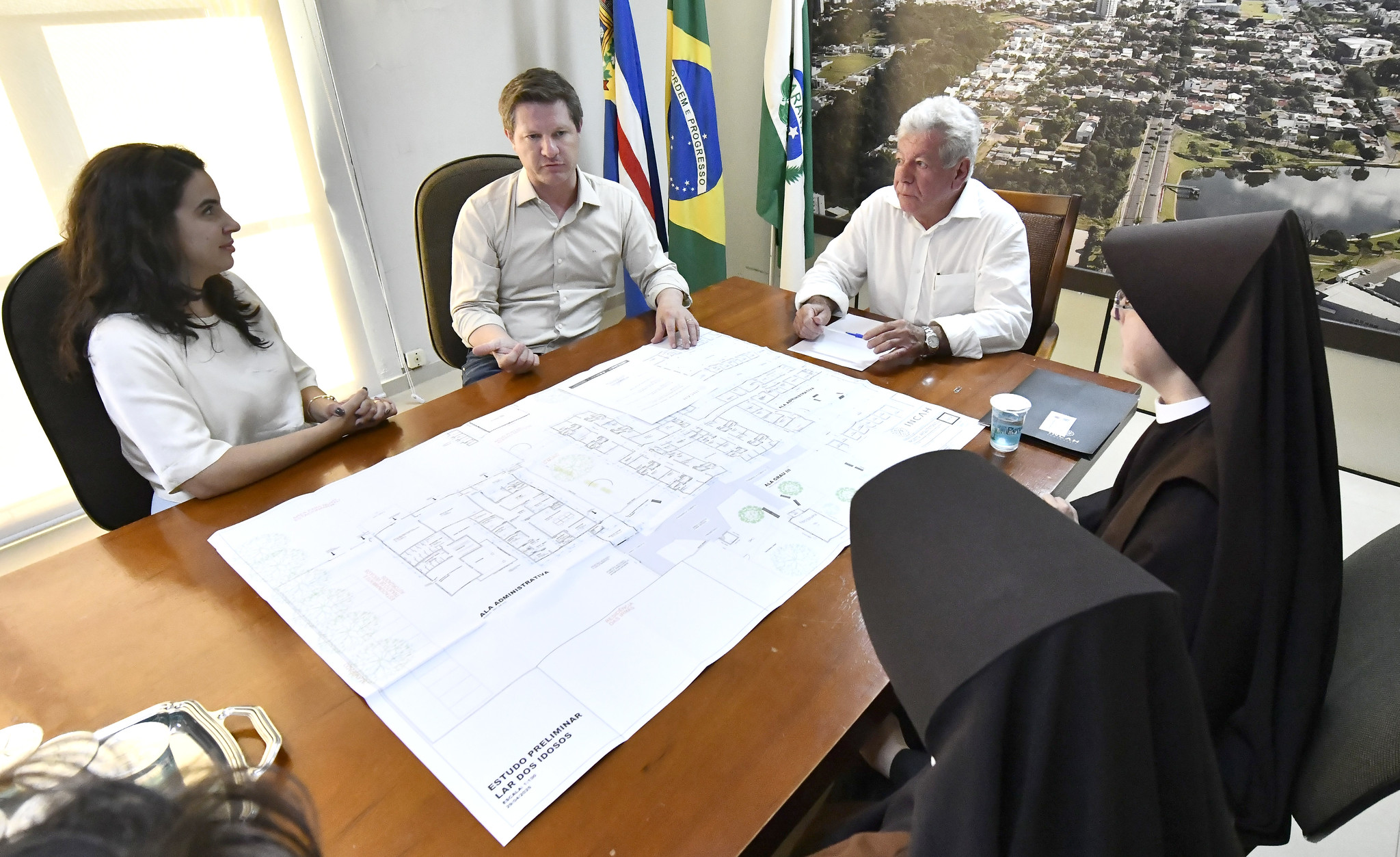 prefeito, secretário e irmãs religiosas reunidos na prefeitura, diante de projeto sobre a mesa