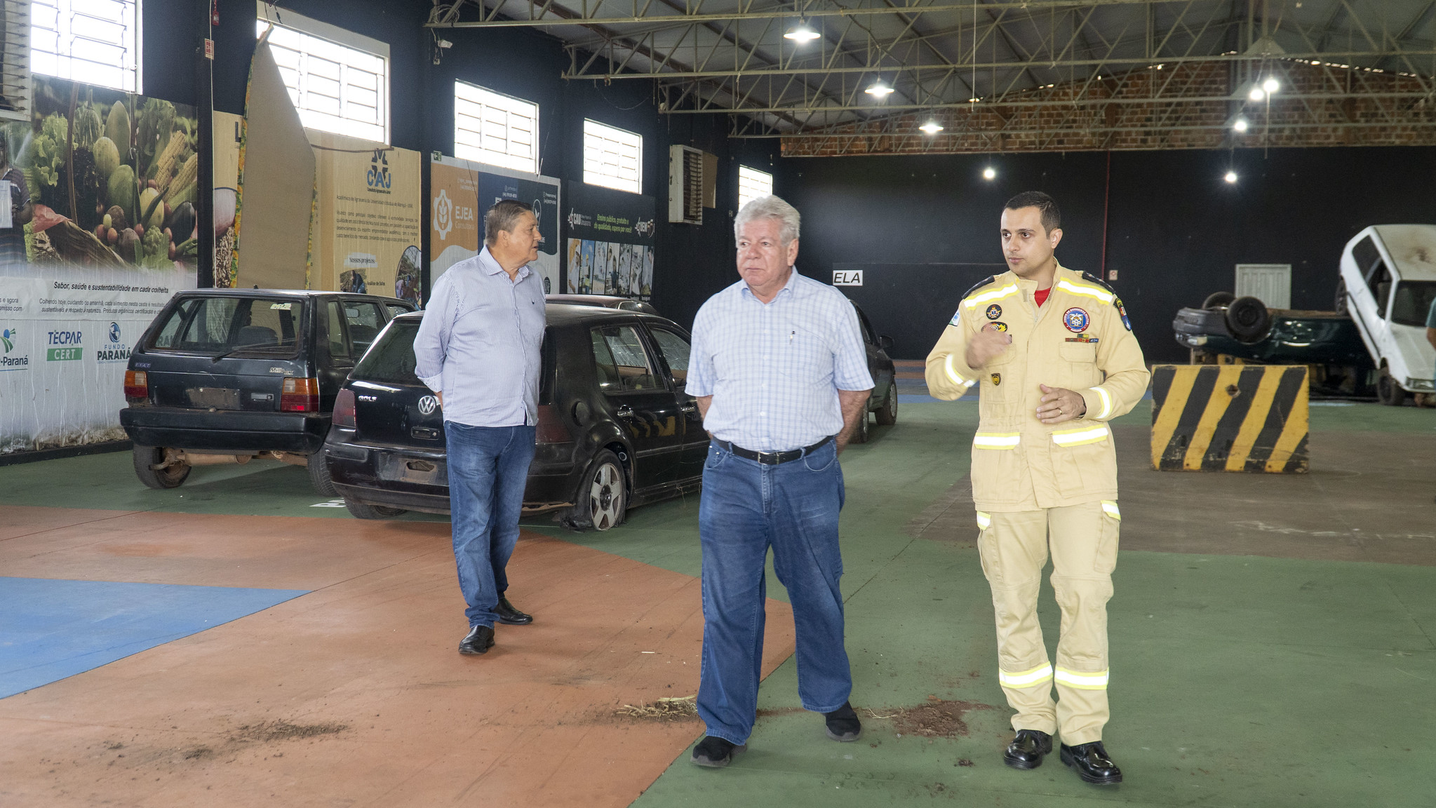 prefeito e bombeiro caminham entre carros batidos que serão usados no treinamento