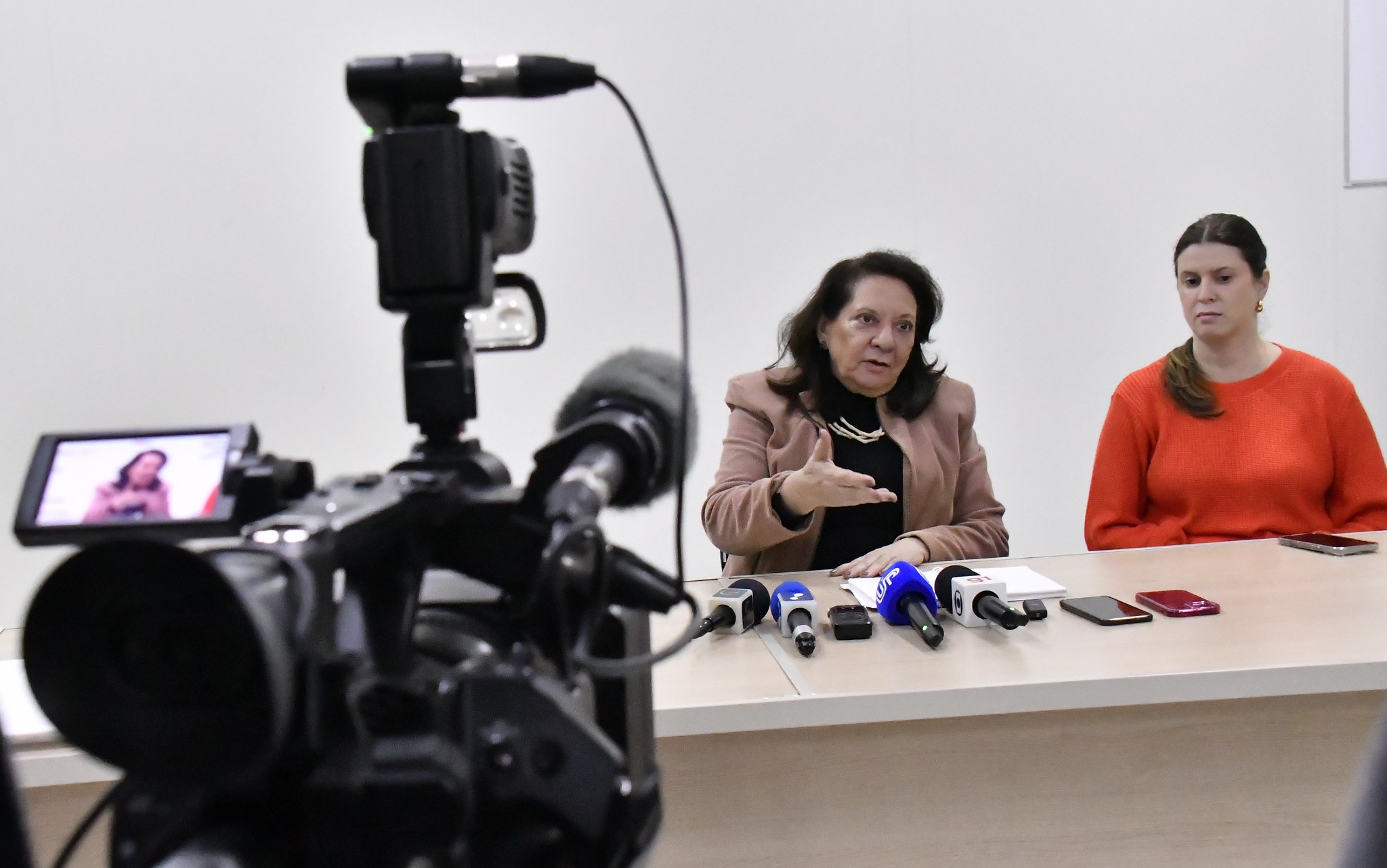 secretaria da saúde fala ao lado da coordenadora do pronto atendimento, sob o foco de uma filmadora