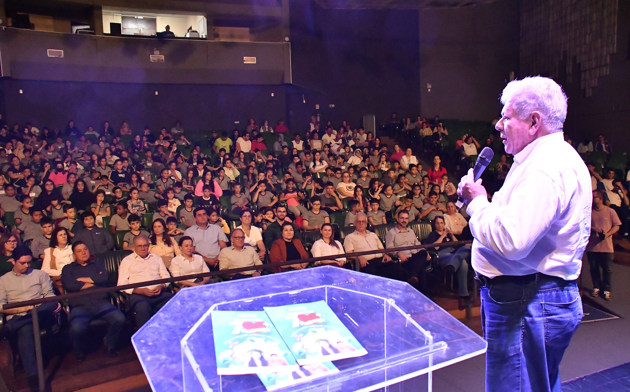 na imagem o prefeito está falando para o auditório lotado de pessoas