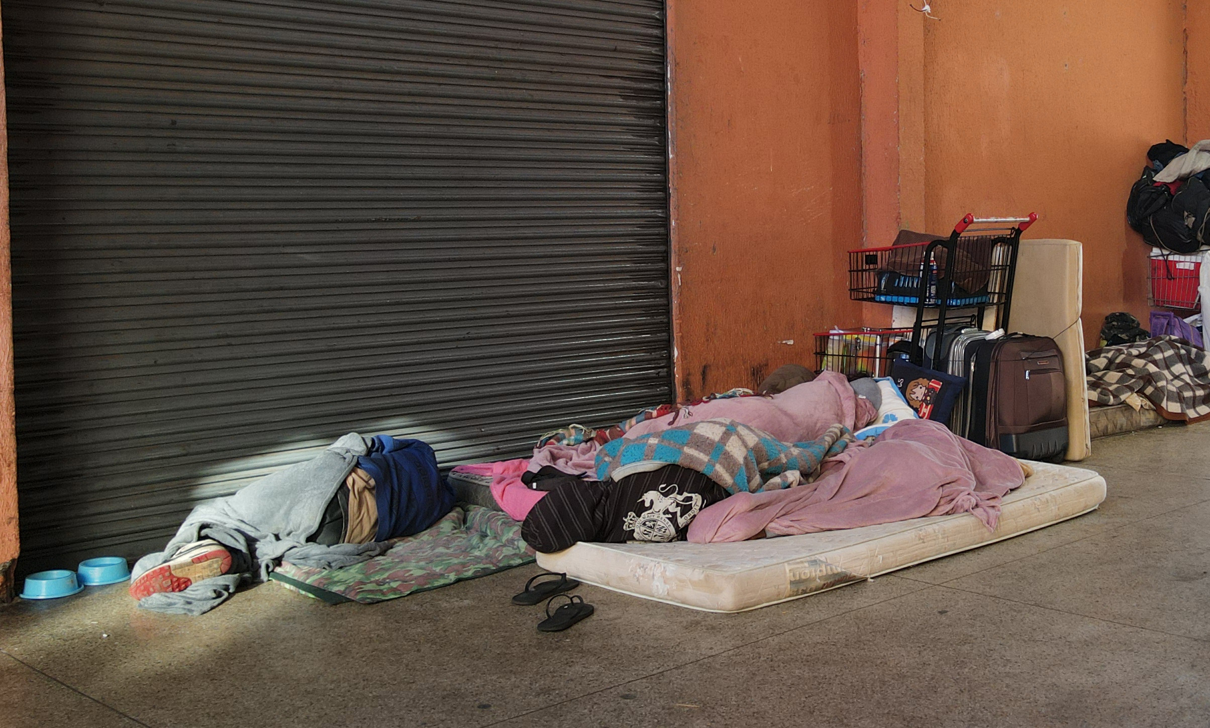 pessoas em situação de rua na imagem, deitadas em calçada e enroladas em cobertores