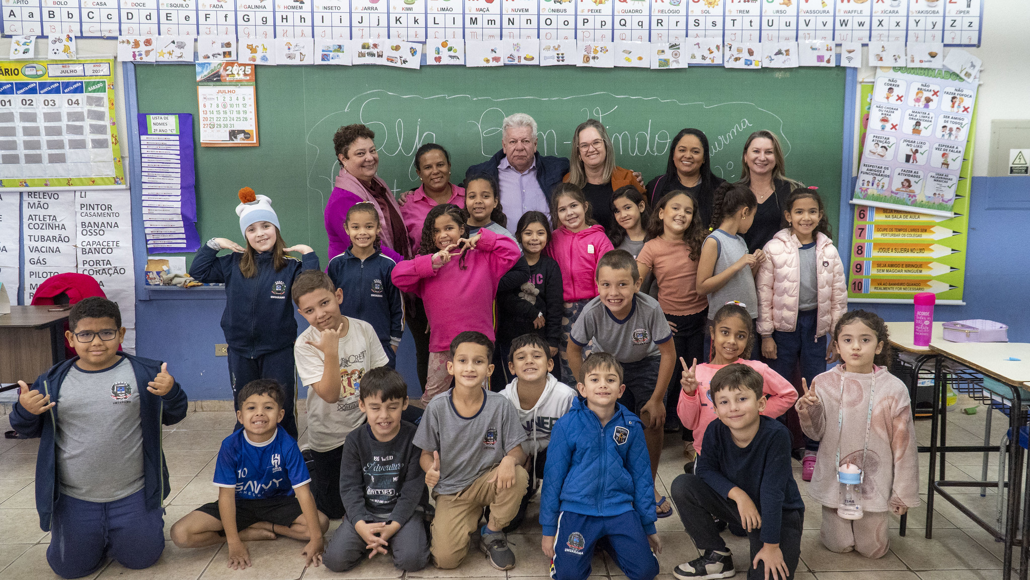 prefeito, professoras e alunas posam para foto na frente do quadro escolar