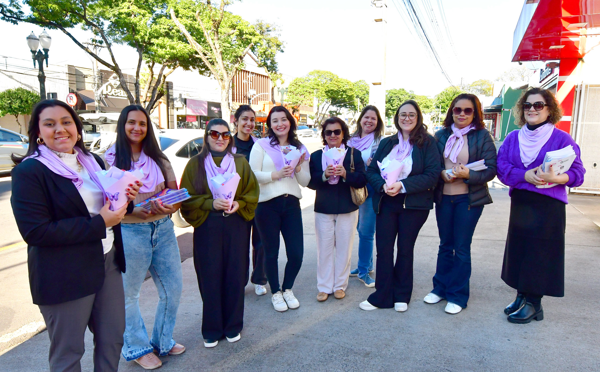 mulheres com lenços da cor lilás distribuem panfletos da campanha para a população
