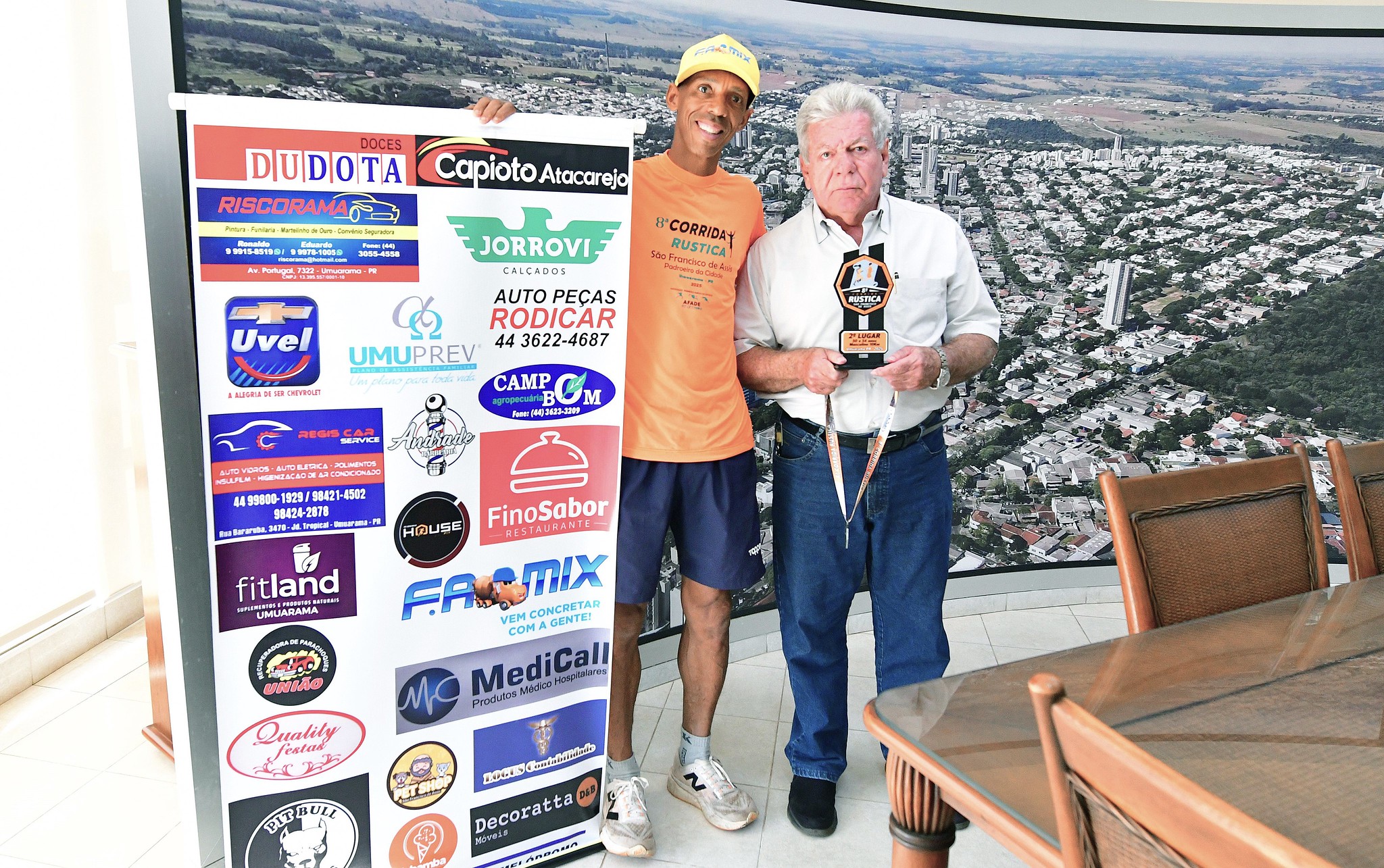 foto do atleta com o prefeito, exibindo troféu, medalha e cartaz com patrocinadores