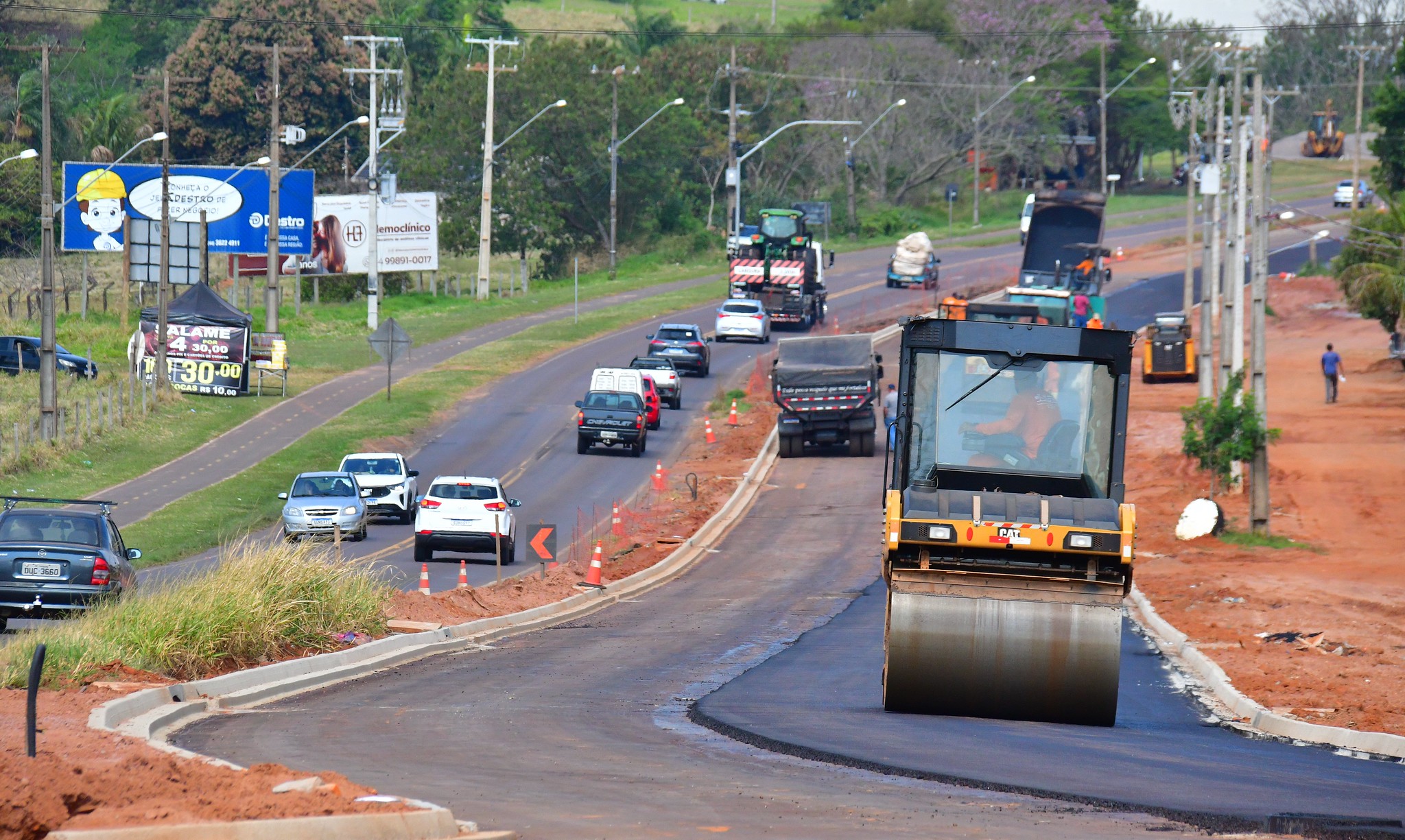 rolo compactando asfalto novo na avenida, com vários carros transitando ao lado