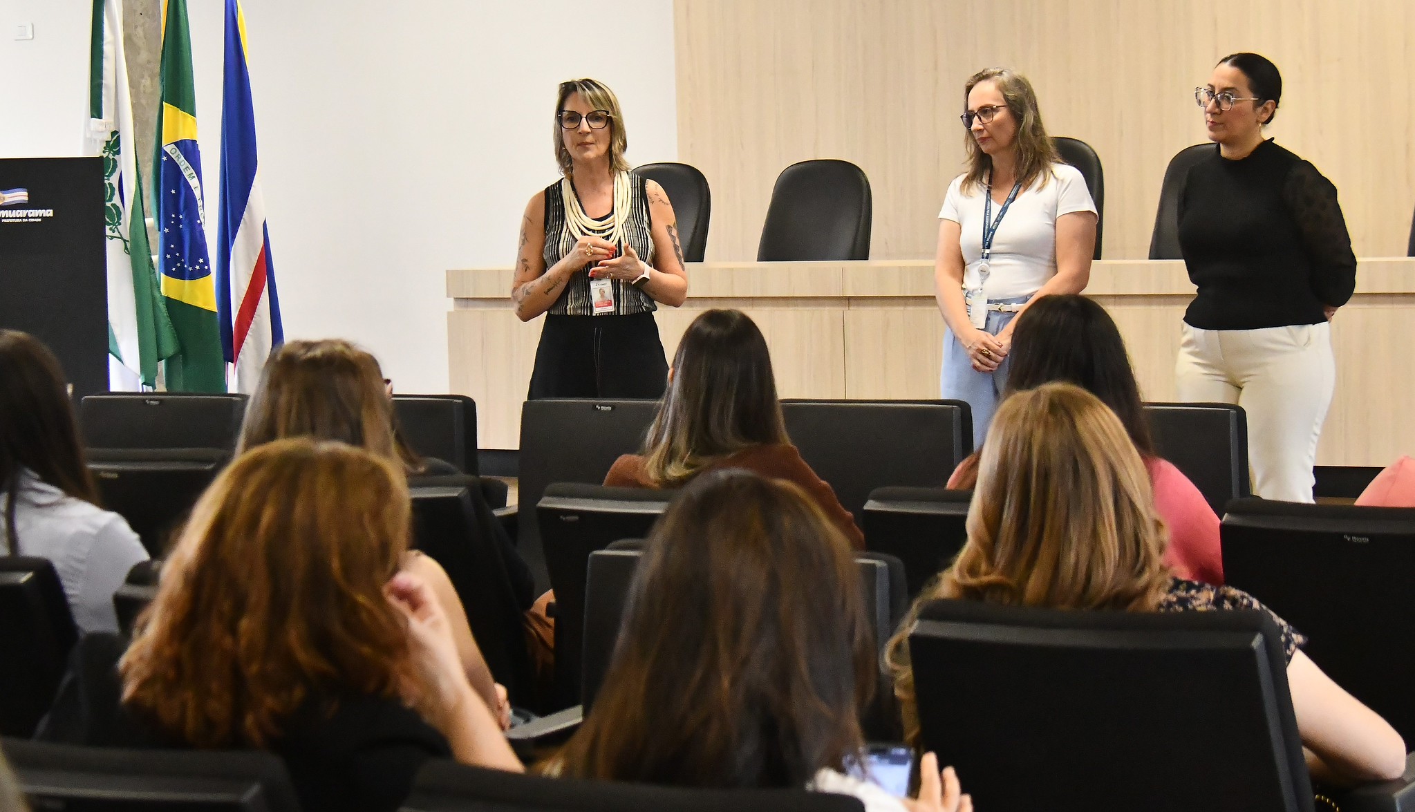 palestrantes falam à frente dos participantes no auditório da Prefeitura