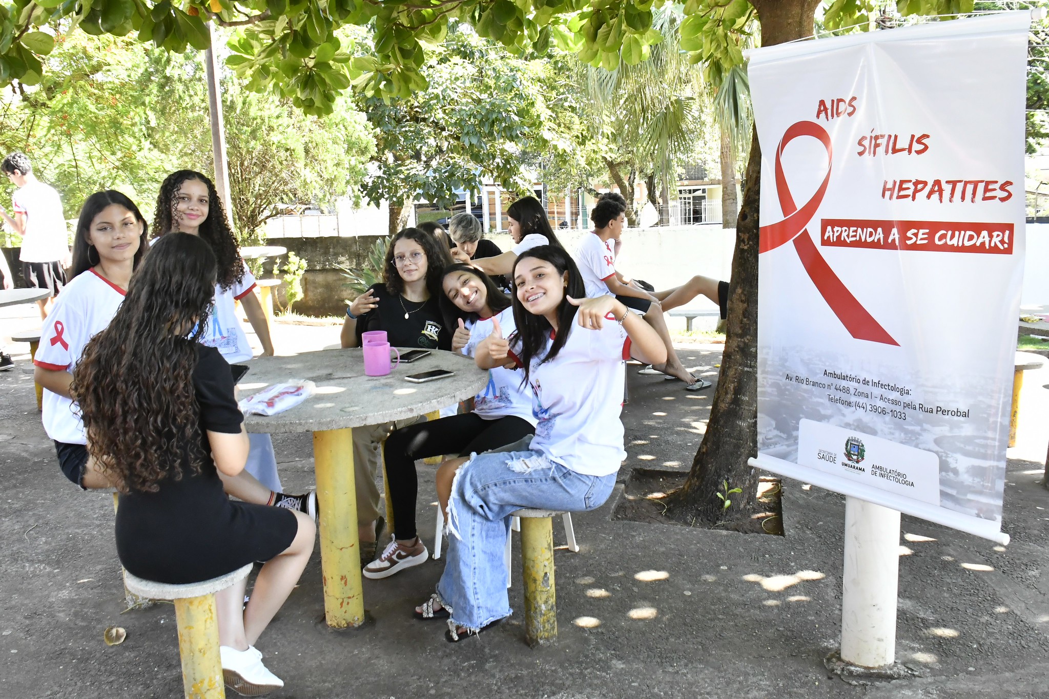 alunos em volta de uma mesa com banner ao lado da campanha realizada há dois anos, contra aids, sífilis e hepatites