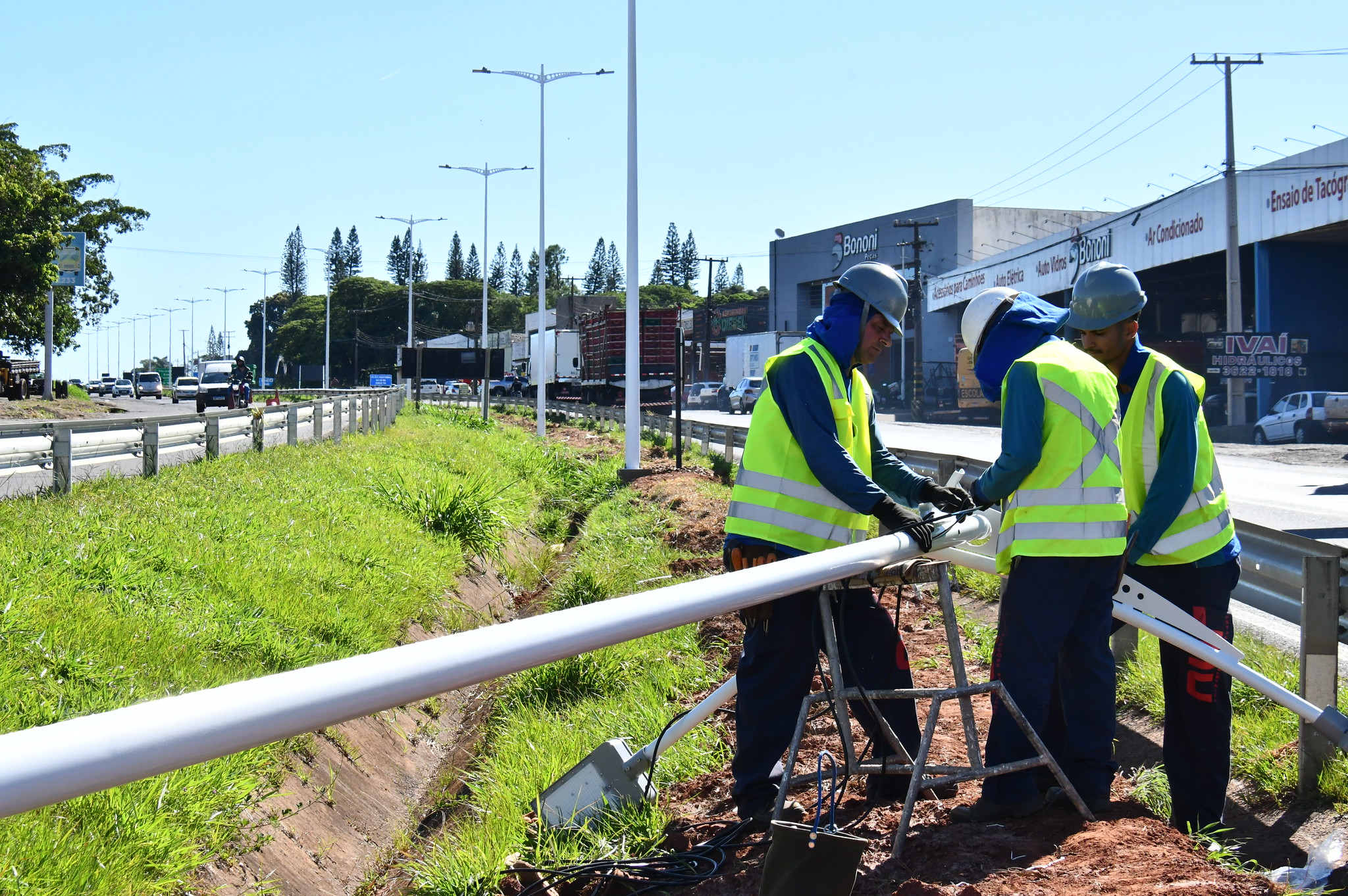 operários instalam postes no canteiro central da rodovia