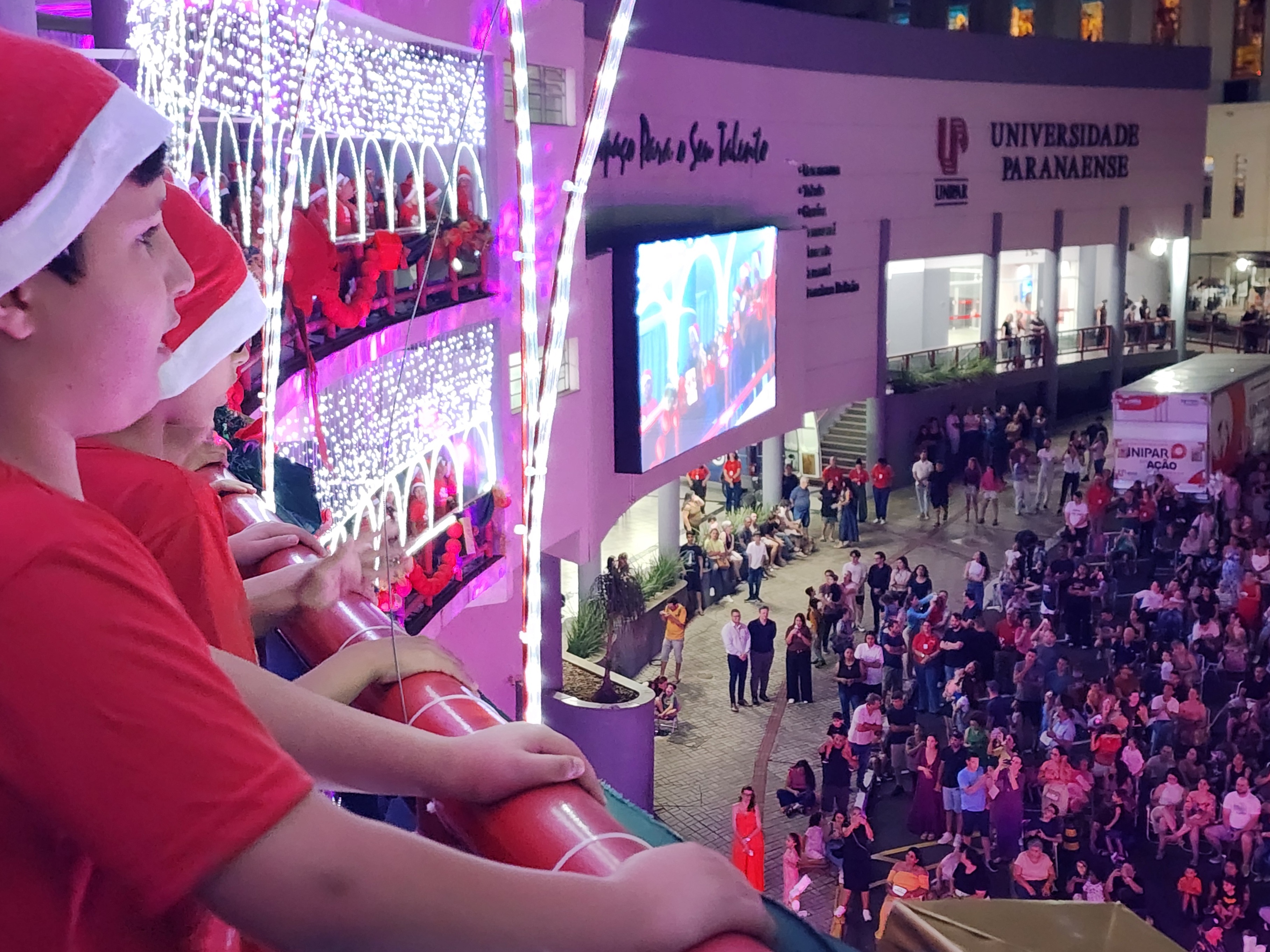 crianças cantam na sacada do prédio, observando o grande público na rua