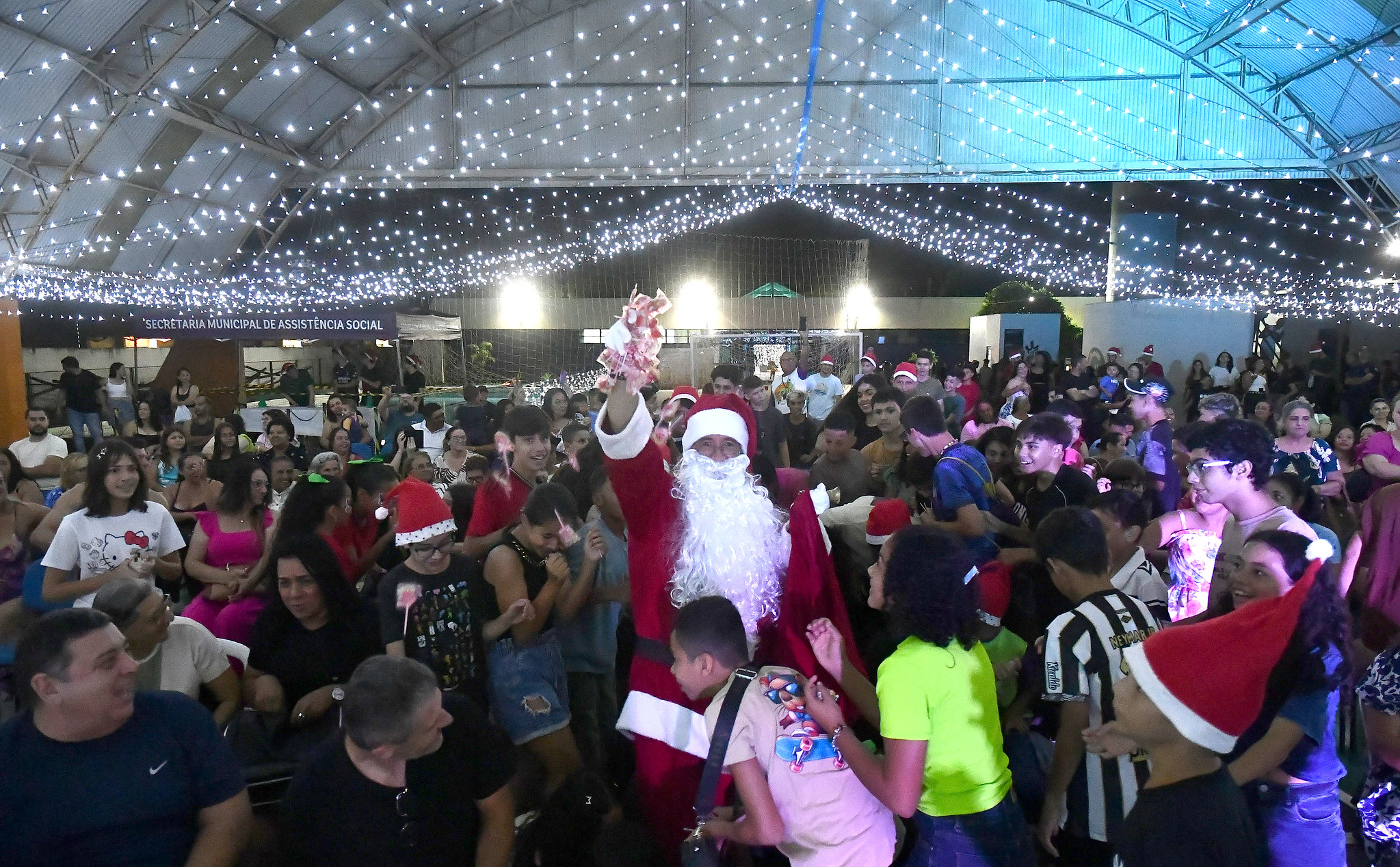 papai noel joga pirulitos para as crianças no local cheio de luzes e alegria