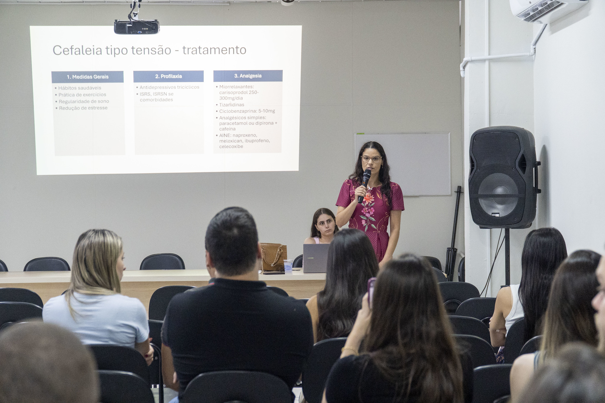 médica neurologista fala aos participantes, acomodados em cadeiras no auditório