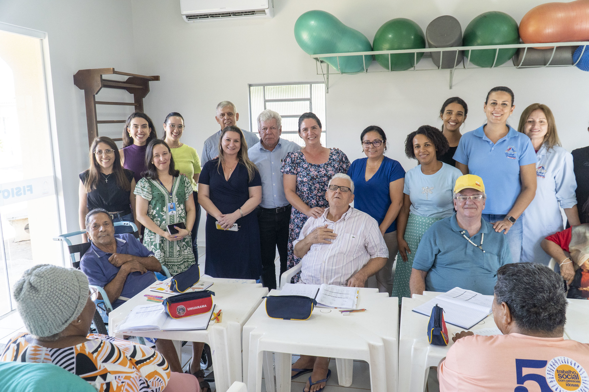 imagem de várias pessoas alinhadas, posando ao lado de idosos que estão estudando