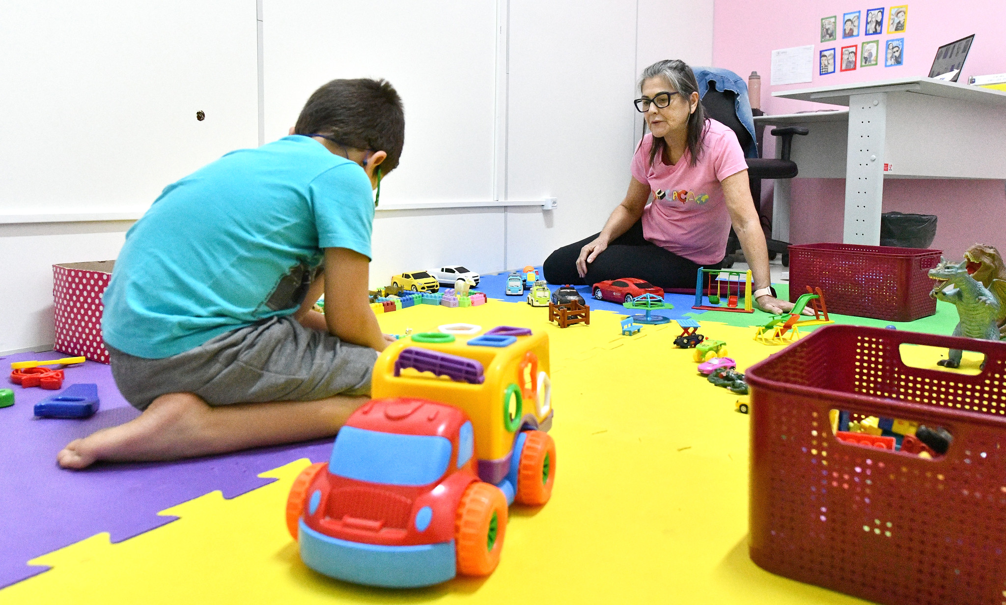 criança brinca em tapete sob a supervisão de cuidadora