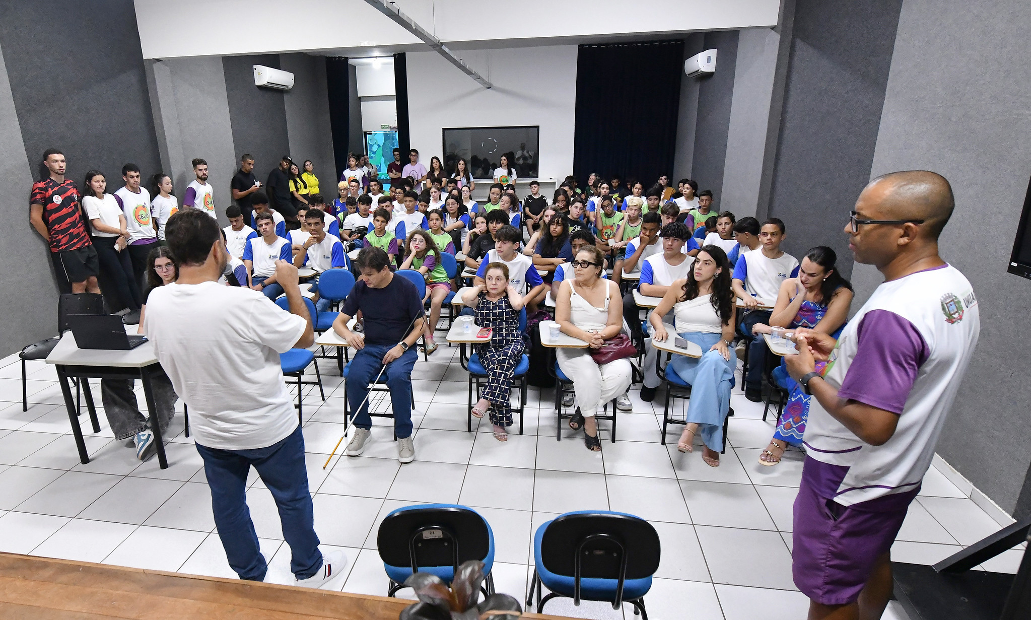 dezenas de jovens reunidos em auditório ouvindo palestra