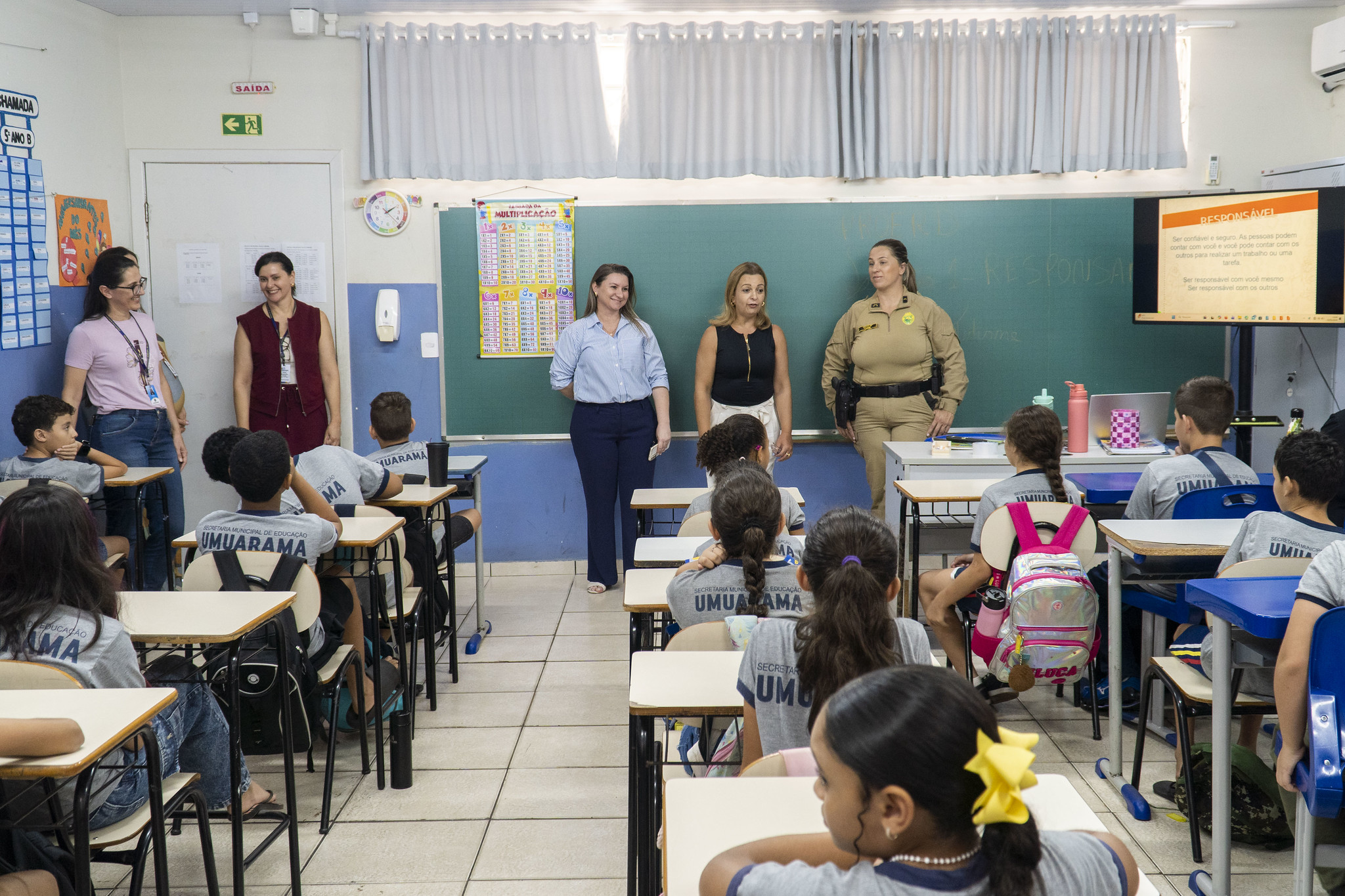 policial visita a sala de aula ao lado de professoras, diante dos alunos