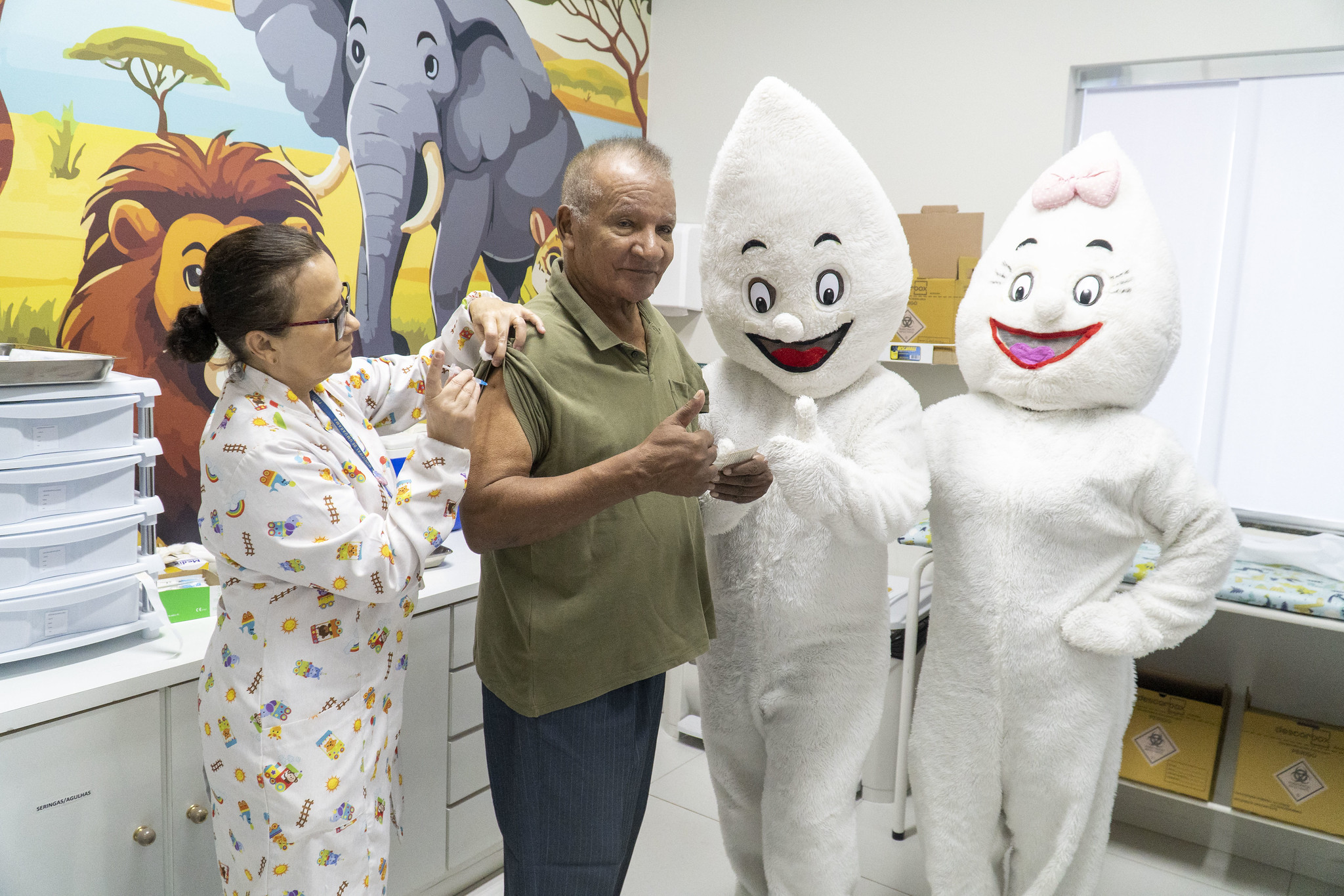 idoso recebe a vacina da gripe no braço, junto com o personagem zé gotinha