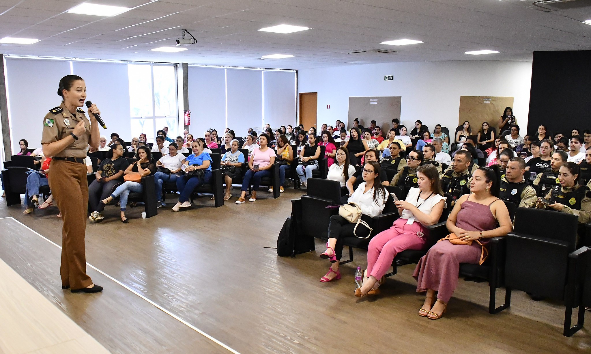 policial militar feminina fala para o auditório cheio de espectadores sentados