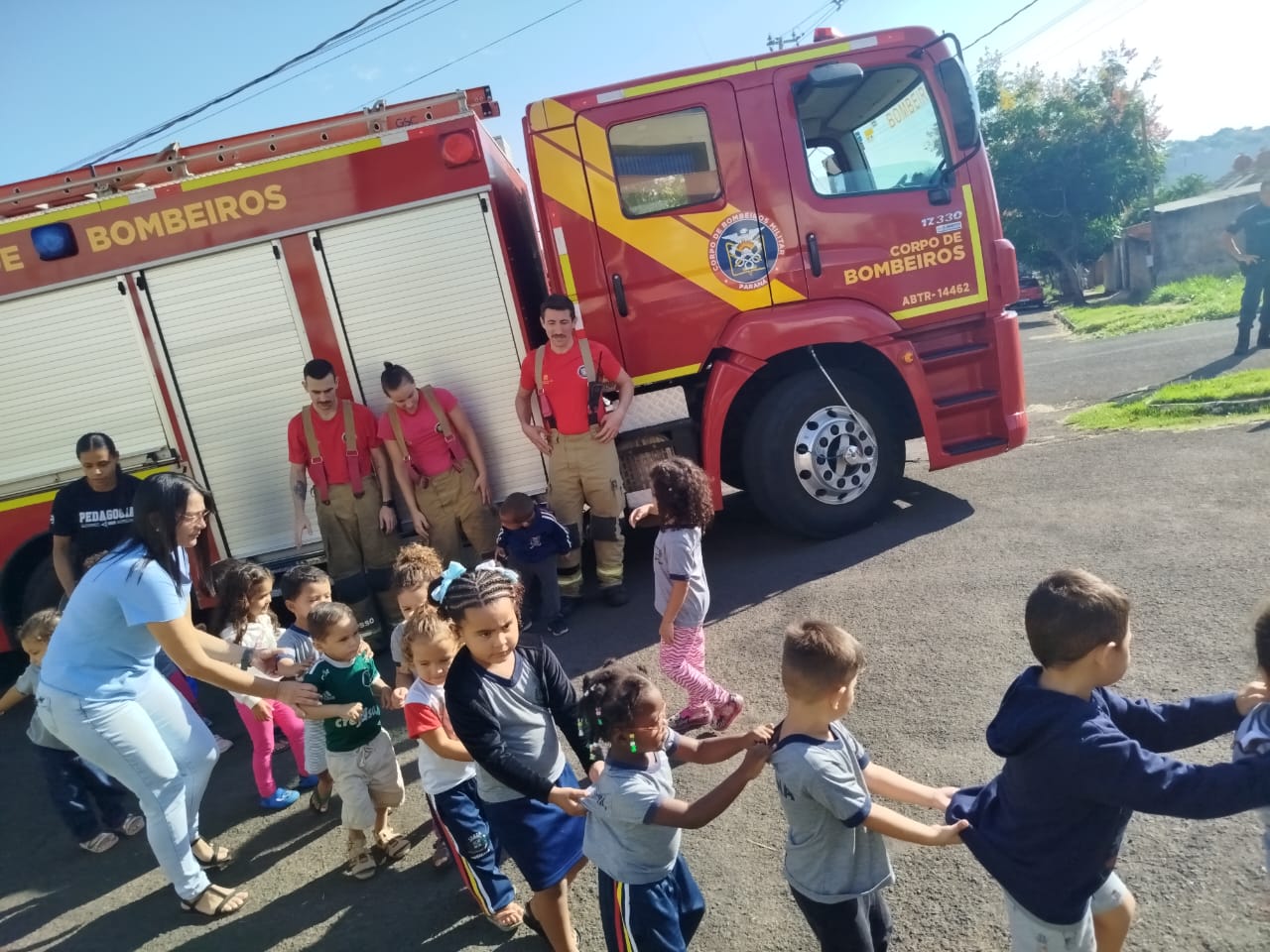crianças em fila são conduzidas para fora da escola, diante do caminhão de bombeiros