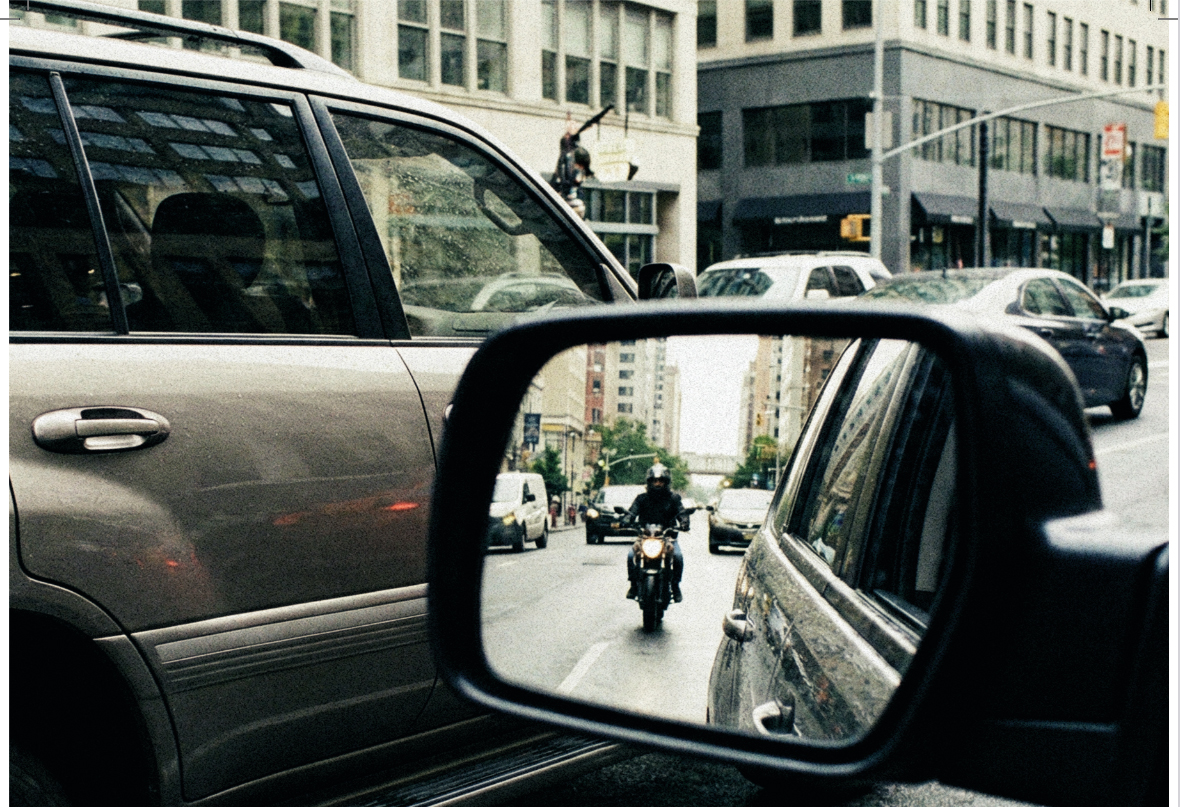 na imagem, retrovisor de veículo no meio do trânsito mostra motocicleta trafegando em seguida