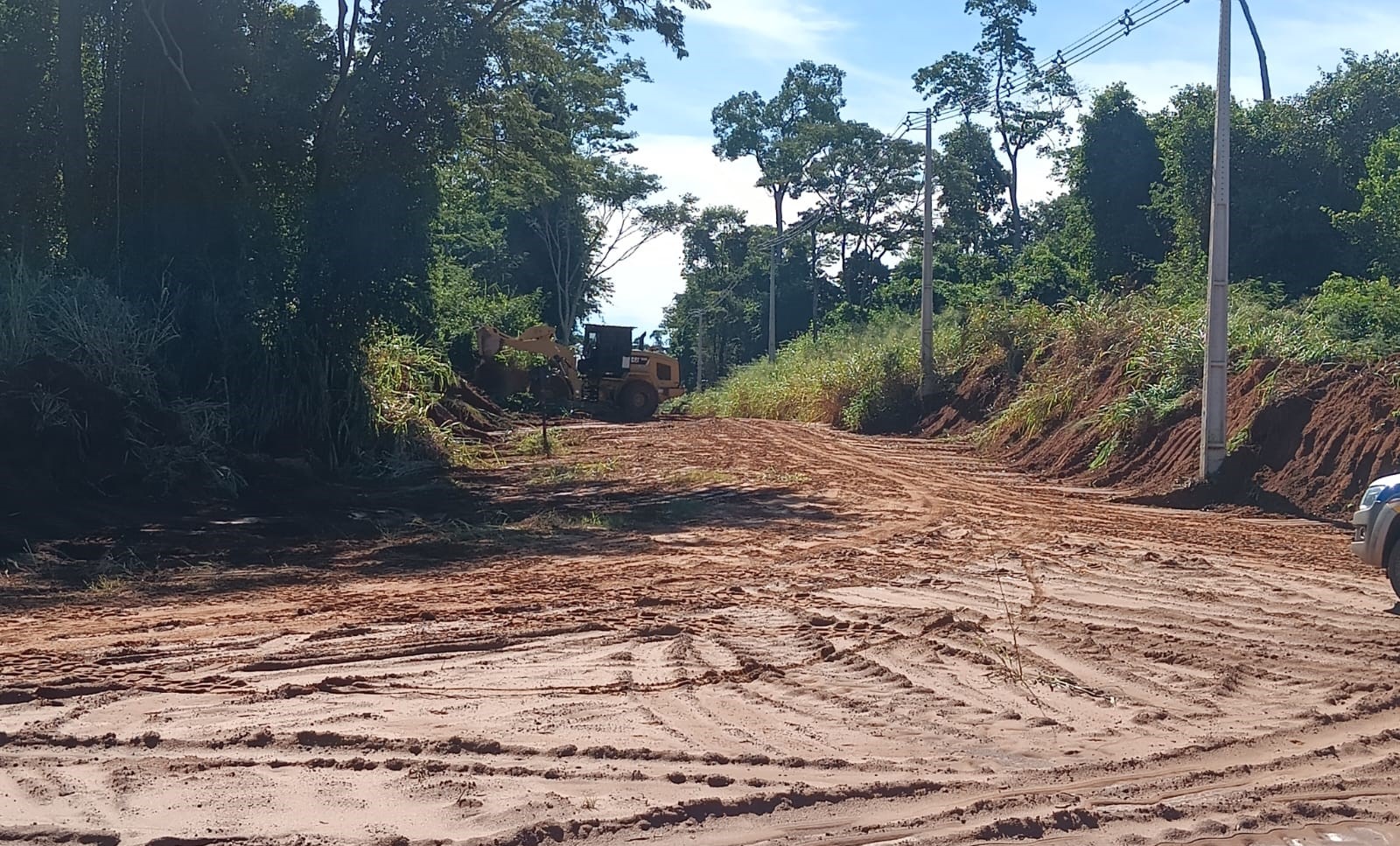 Máquina pá-carregadeira faz limpeza de mato à margem de estrada rural