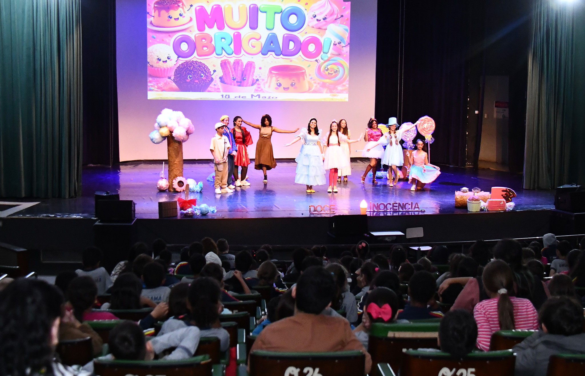 artistas se apresentam no palco diante das crianças na plateia