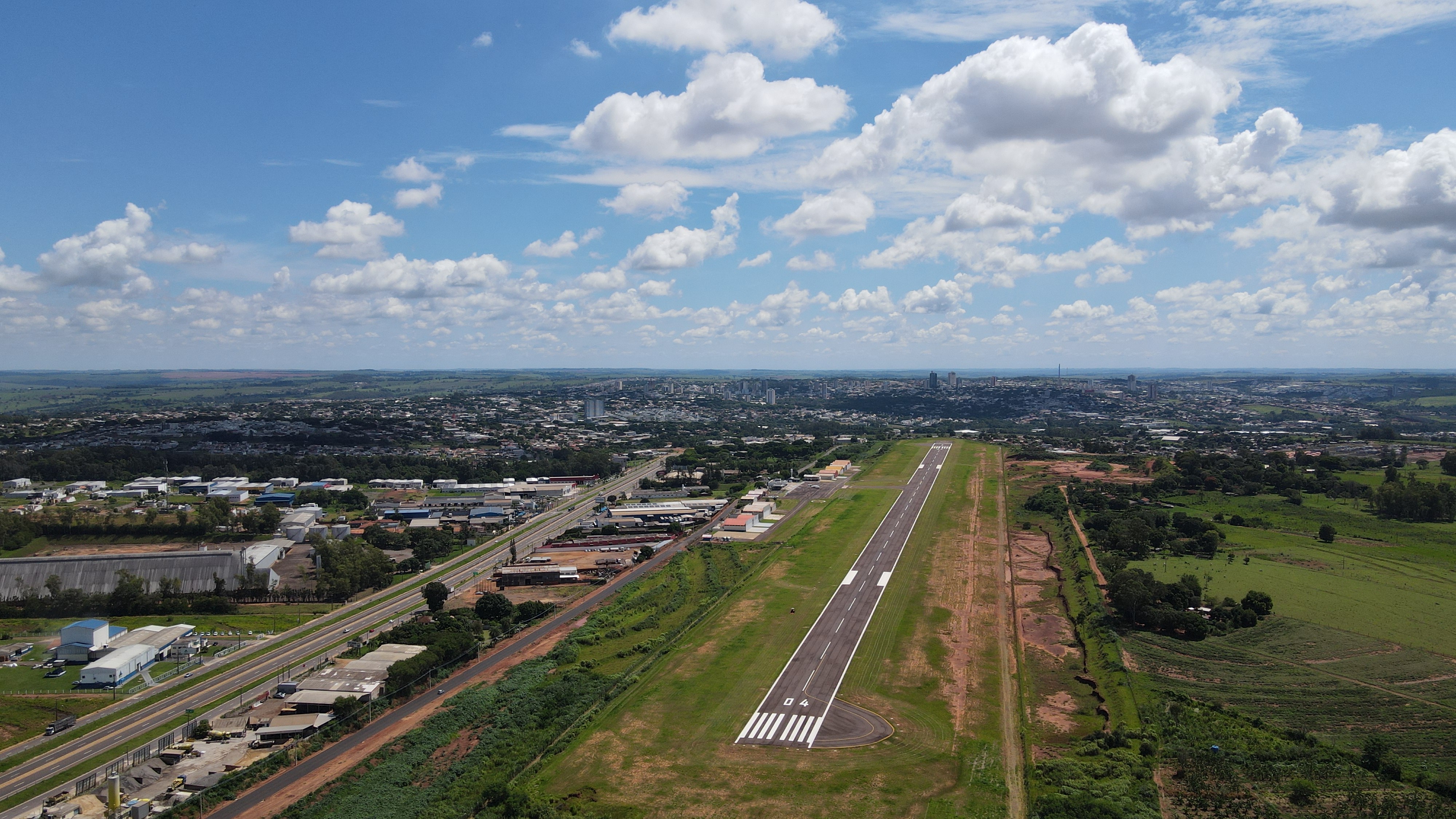imagem aérea do aeroporto, com a cidade ao fundo e um céu azul com algumas nuvens