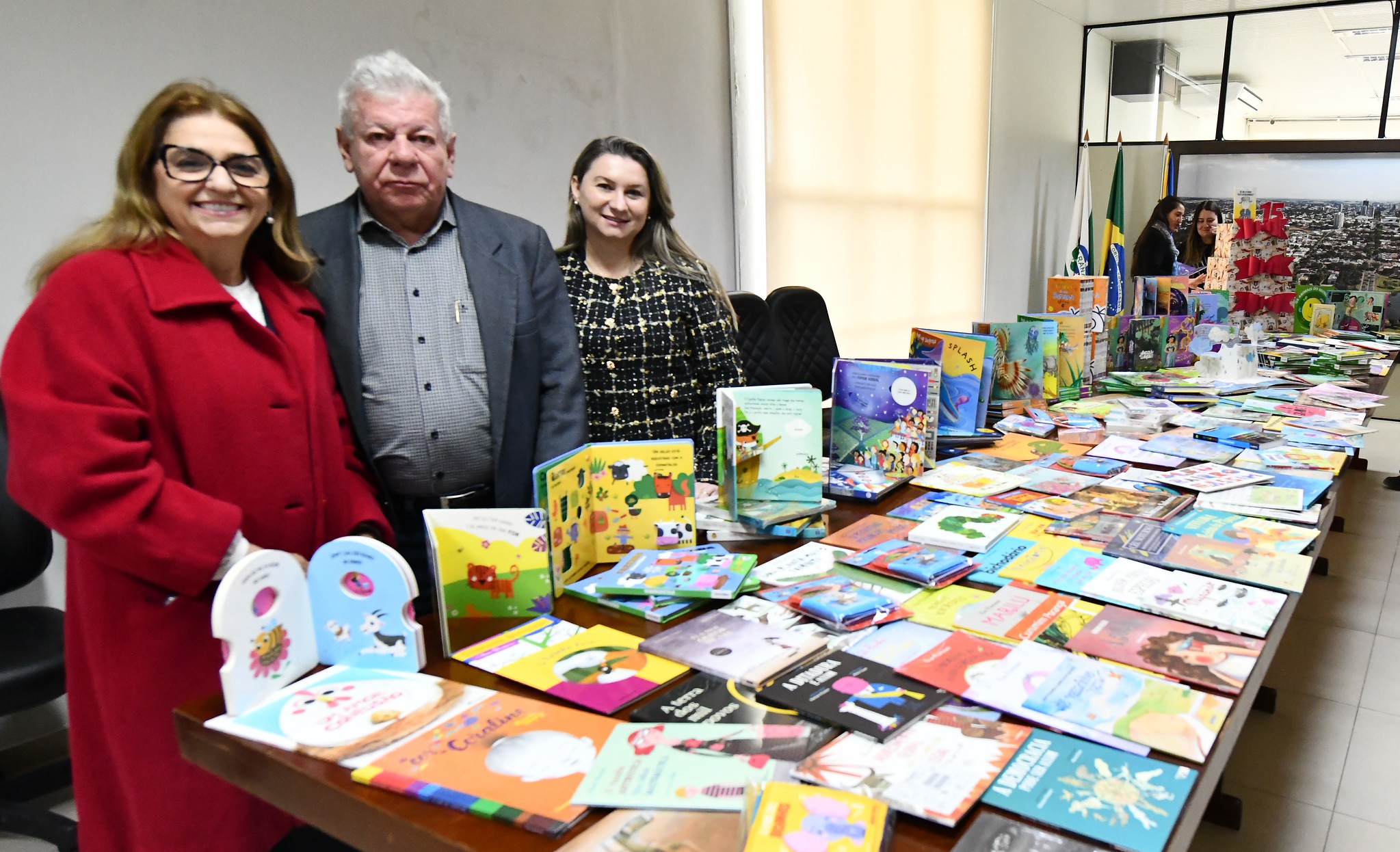 prefeito e professoras ao lado dos livros, espalhados em uma mesa