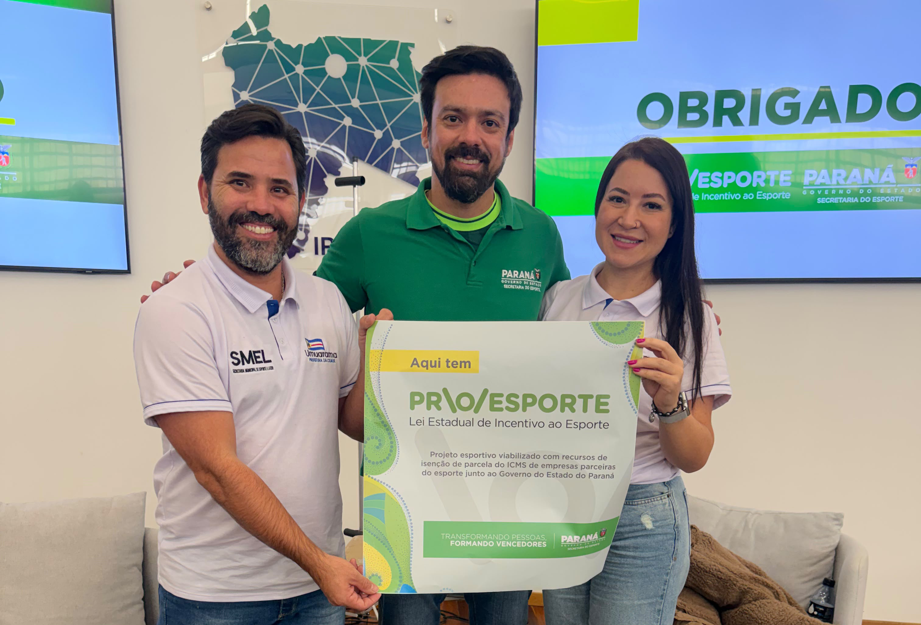 três pessoas seguram cartaz com nome do programa