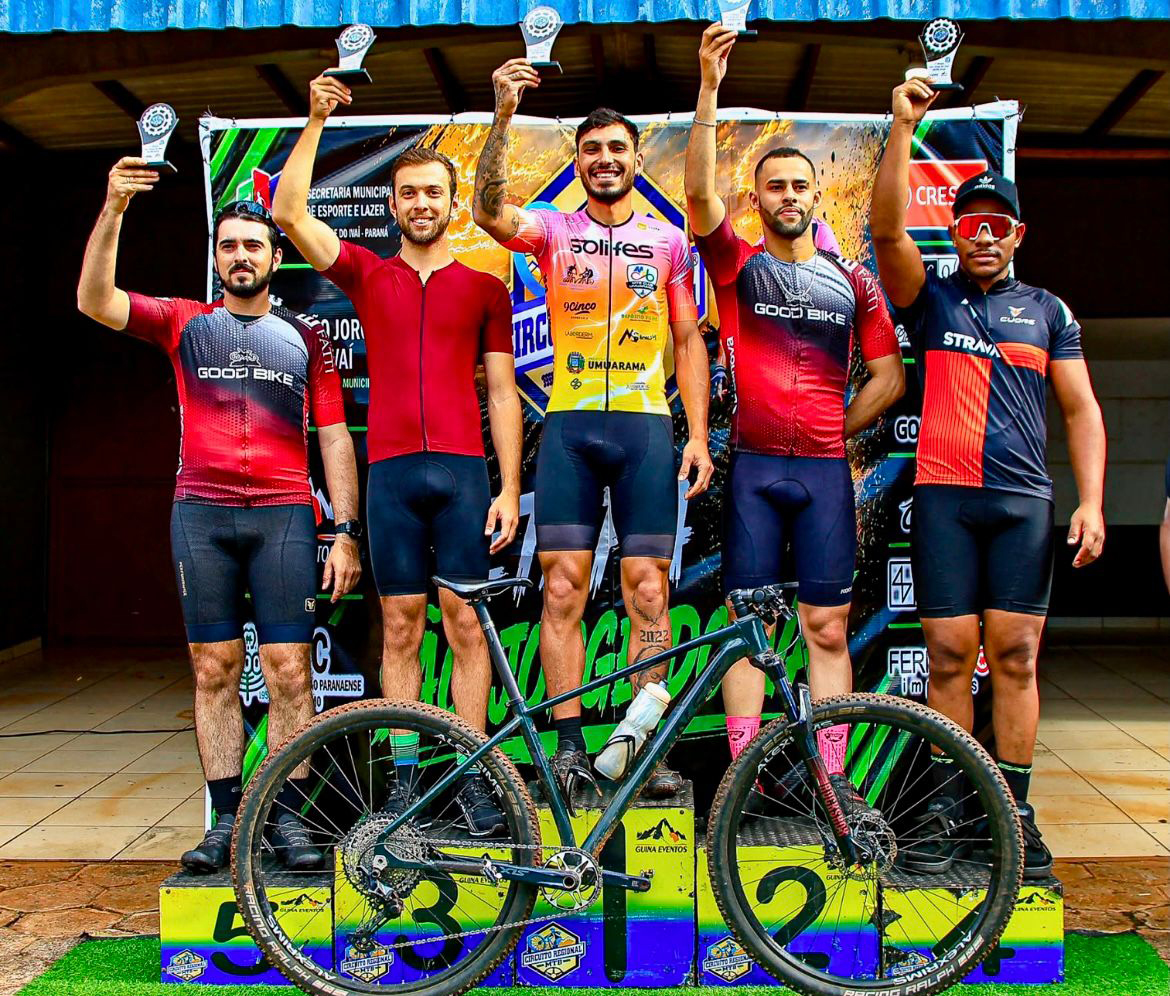 pilotos de ciclismo no pódio com troféus e uma bicicleta na frente