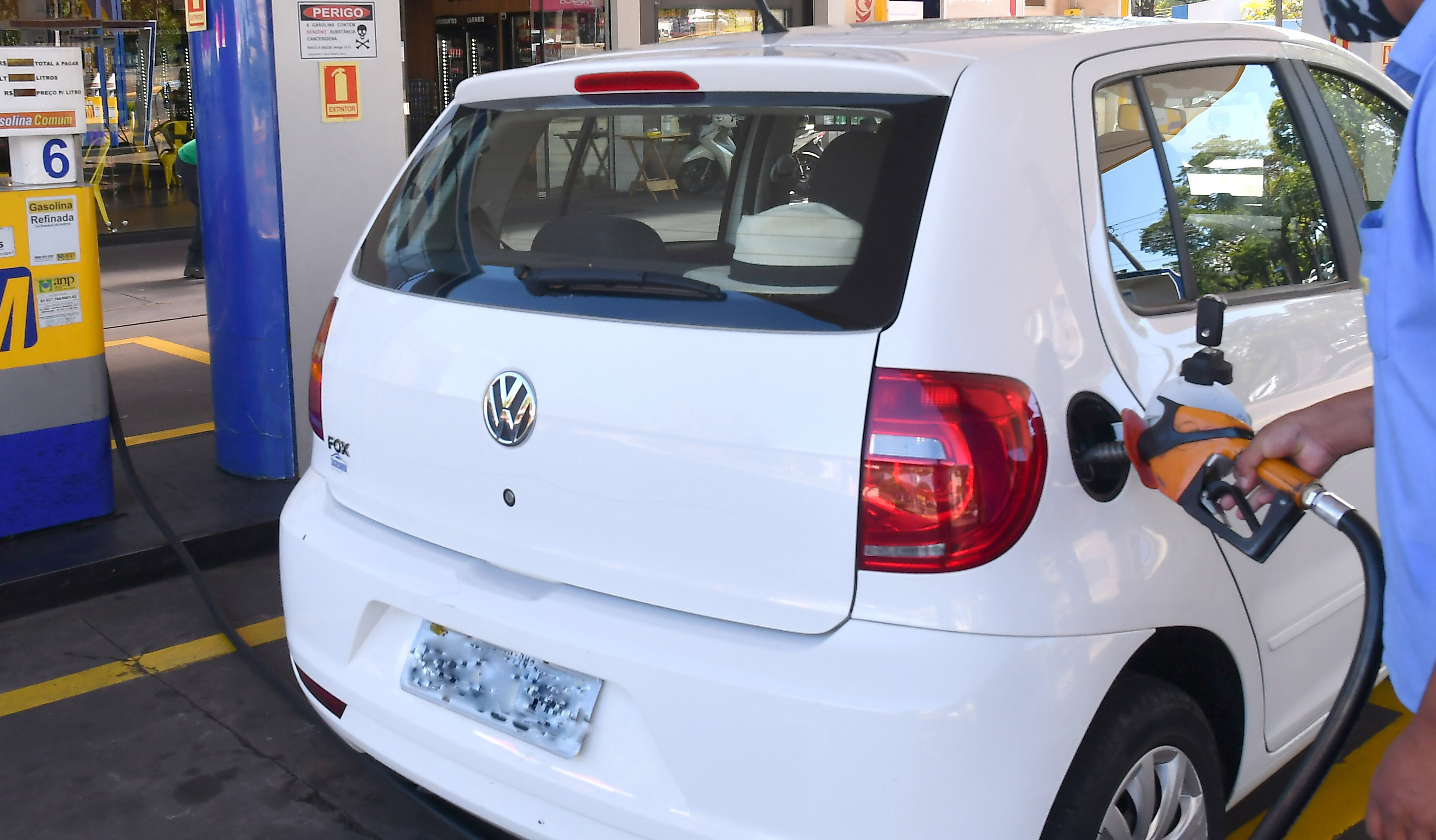 frentista abastece carro branco em posto de combustíveis