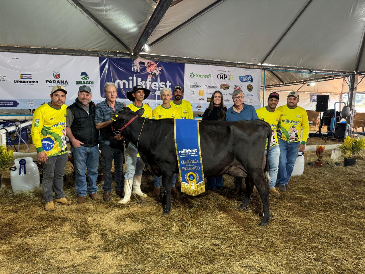 vaca com flâmula de campeã à frente dos criadores e julgadores