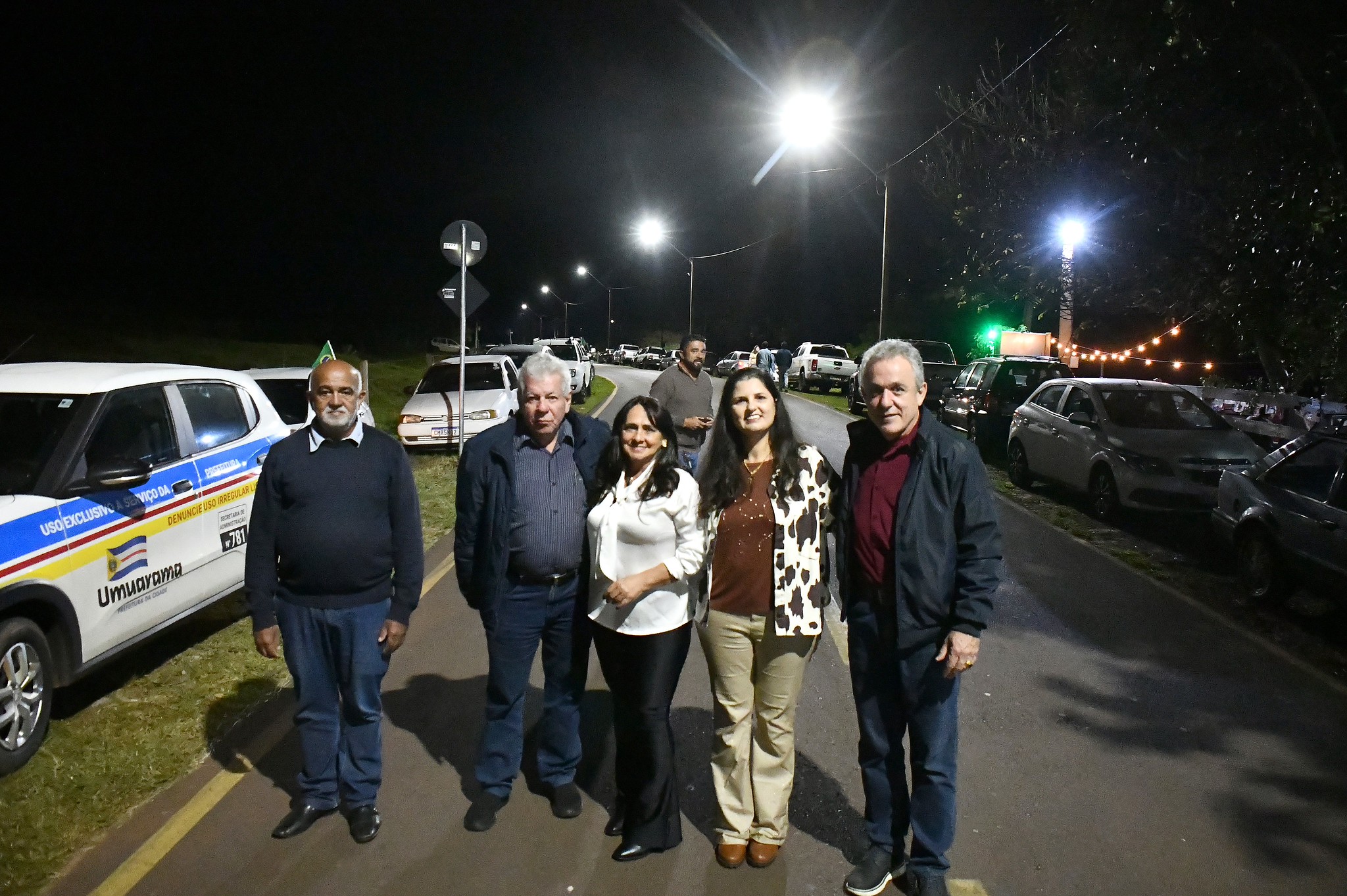 pessoas na frente de uma estrada rural asfaltada e iluminada com lâmpadas LED