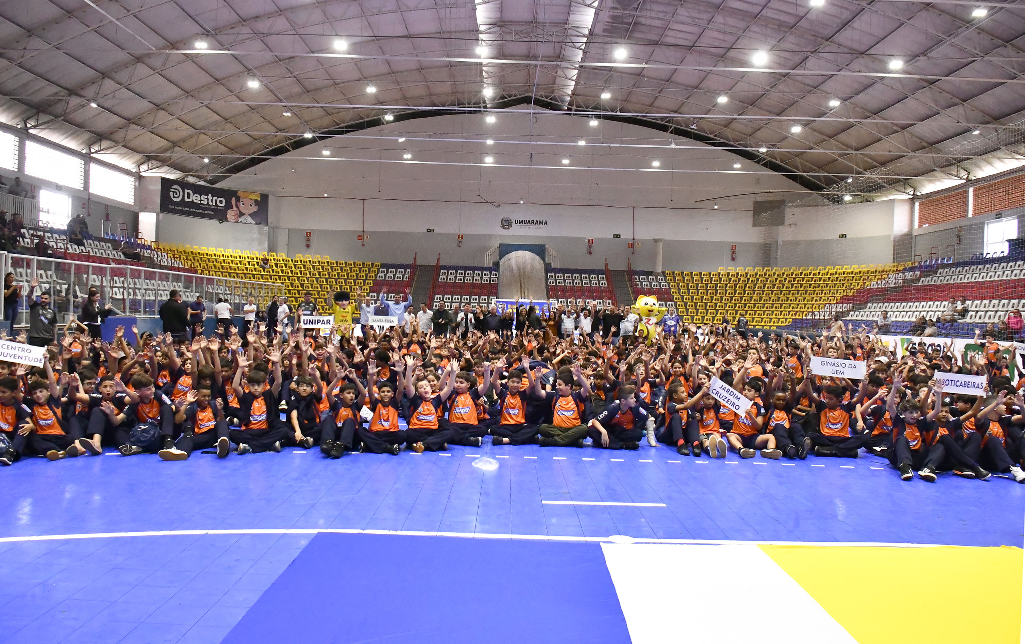 Imagem na quadra do ginásio de esportes com todos os alunos da Afsu em primeiro plano e autoridades em segundo plano ao fundo, para a entrega dos kits esportivos a 726 alunos e adolescentes