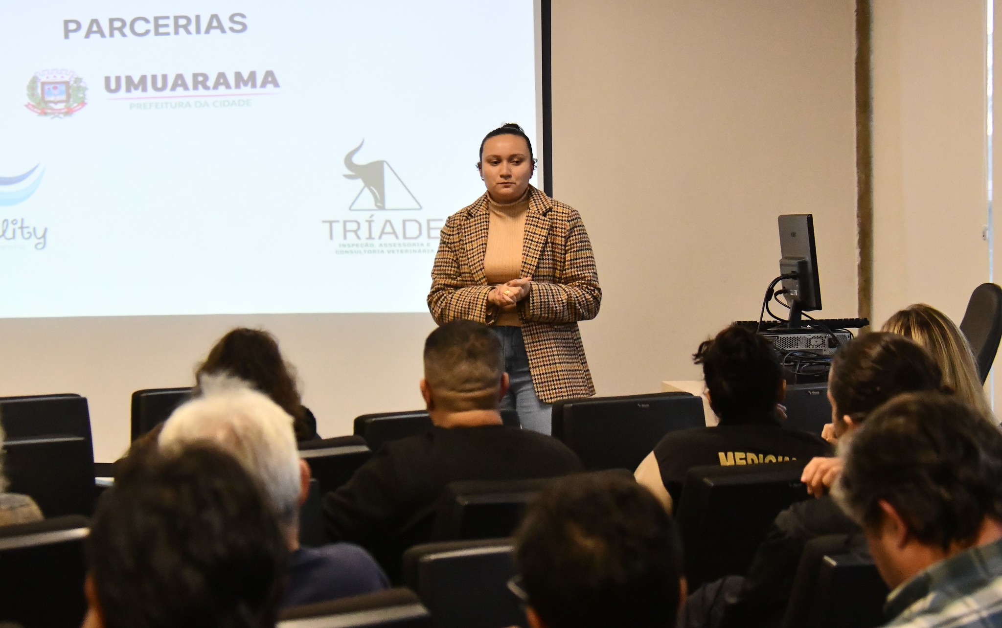 Palestra destinada a profissionais que atuam com  manipulação de carnes. Na imagem a palestrante de frente para os participantes que aparecem de costas no auditório