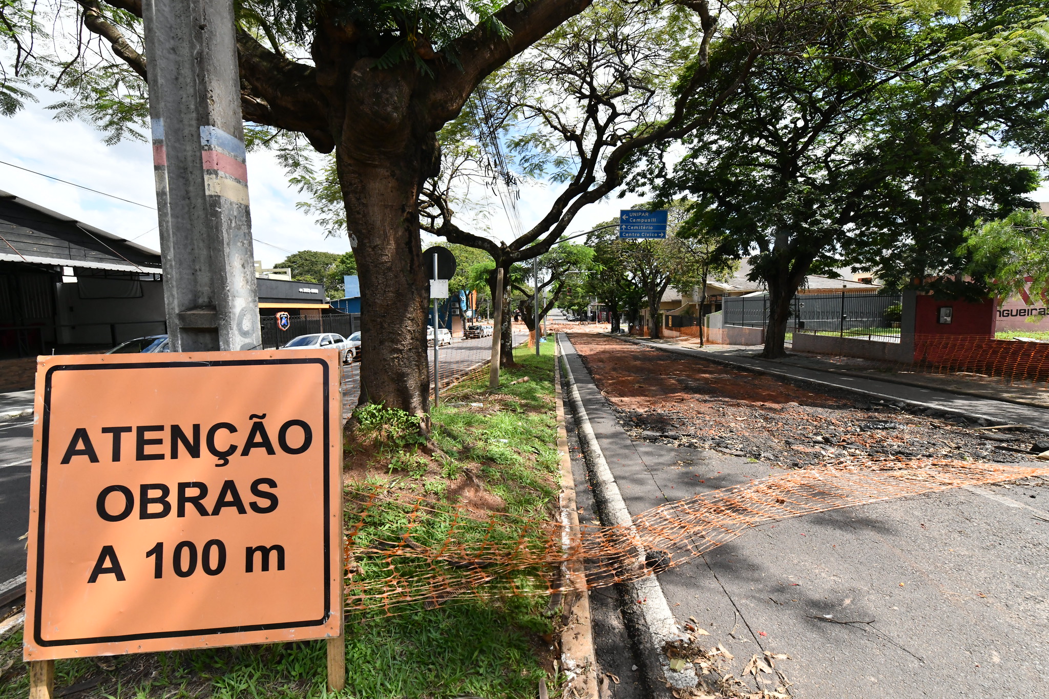 placa de obras ao lado de rua com asfalto descascado