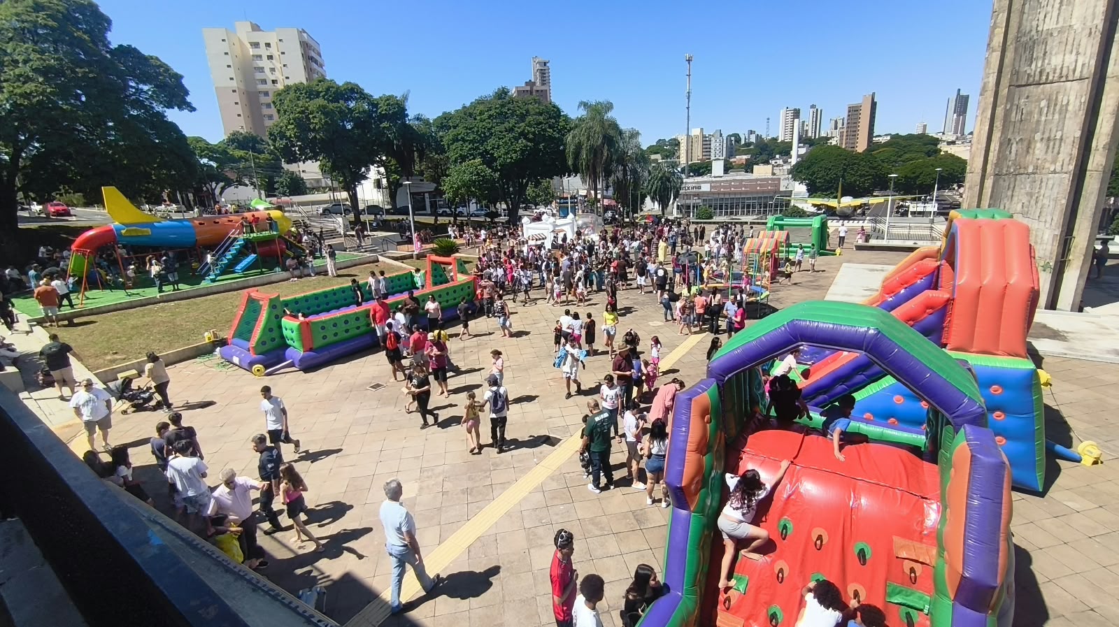 imagem geral da praça, com o público presente e os brinquedos
