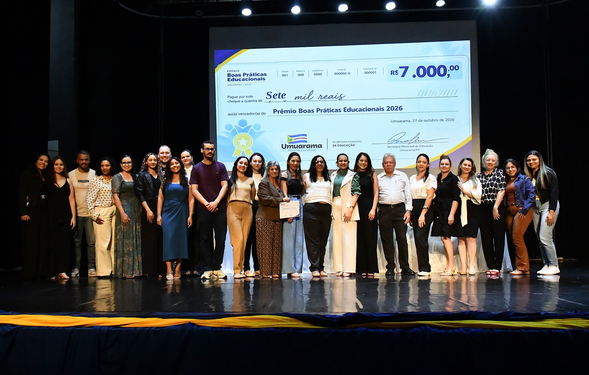 professores premiados no palco, ao fundo uma imagem do prêmio em dinheiro